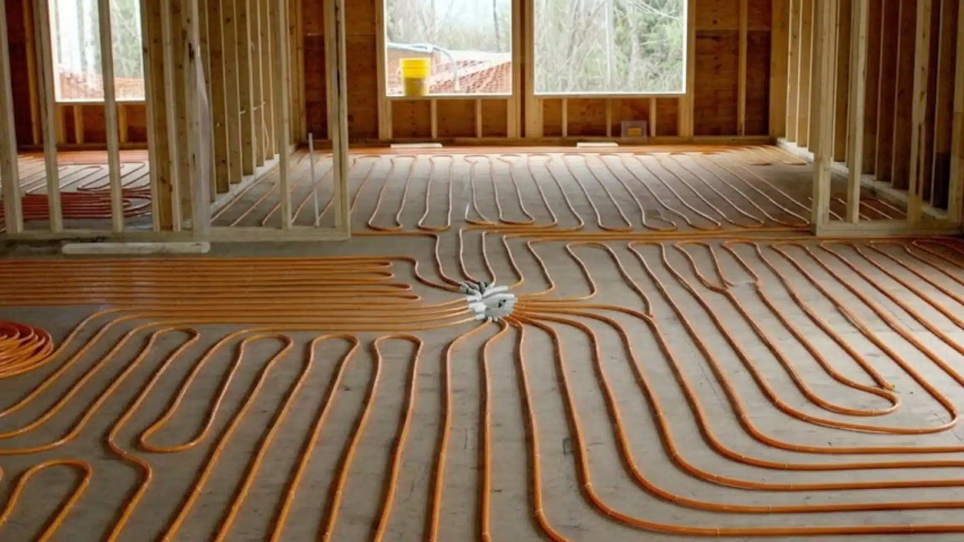 Orange radiant heating pipes arranged in serpentine loops across a concrete floor in a house under construction