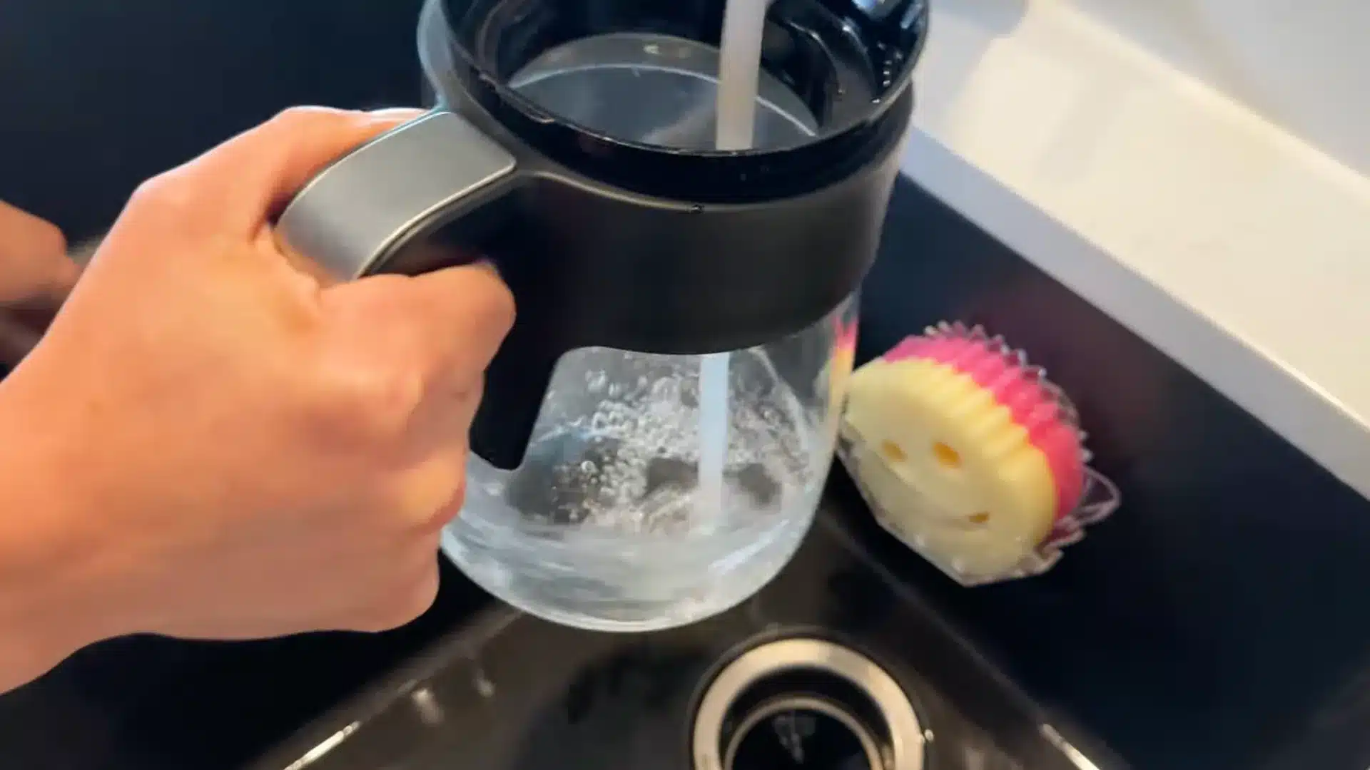 Rinsing coffee maker carafe under running water in kitchen sink after cleaning cycle