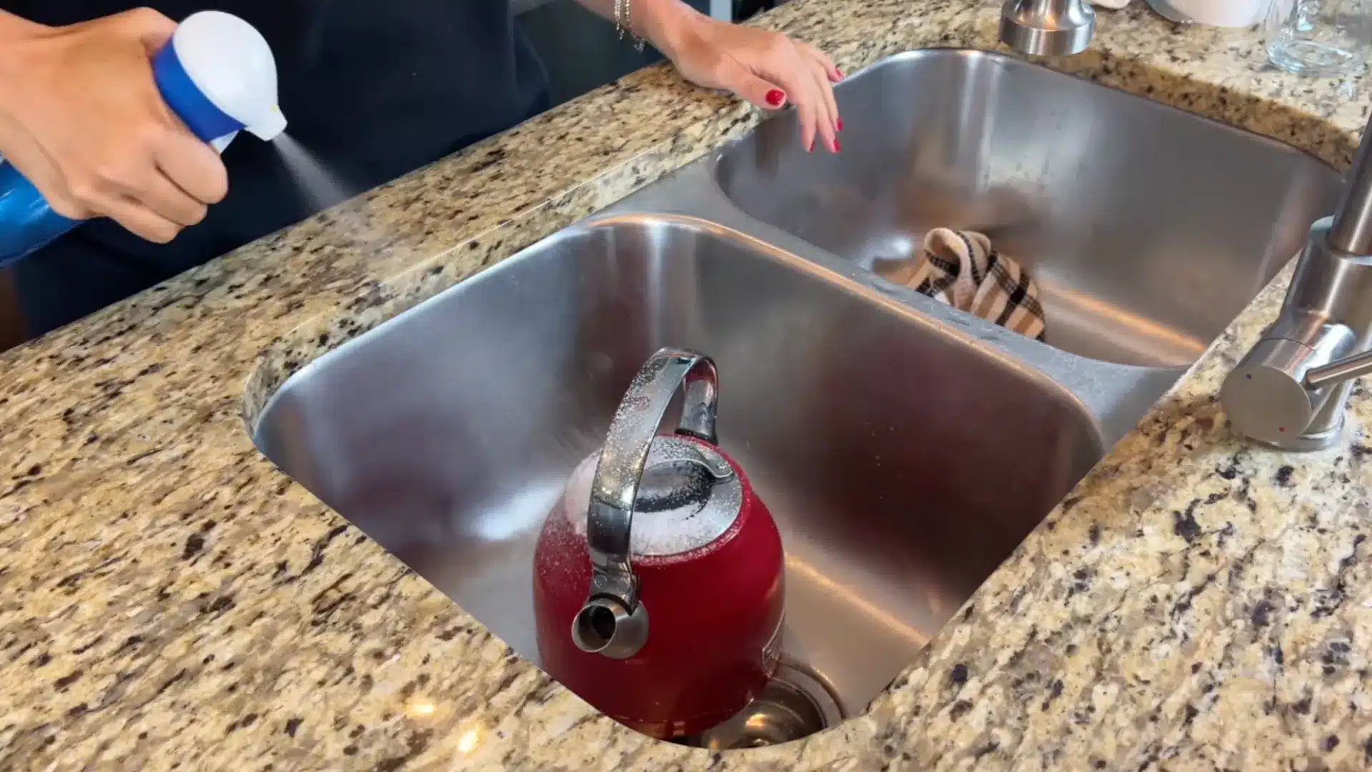 Spraying cleaner on the outside of a red kettle to remove grease and kitchen buildup