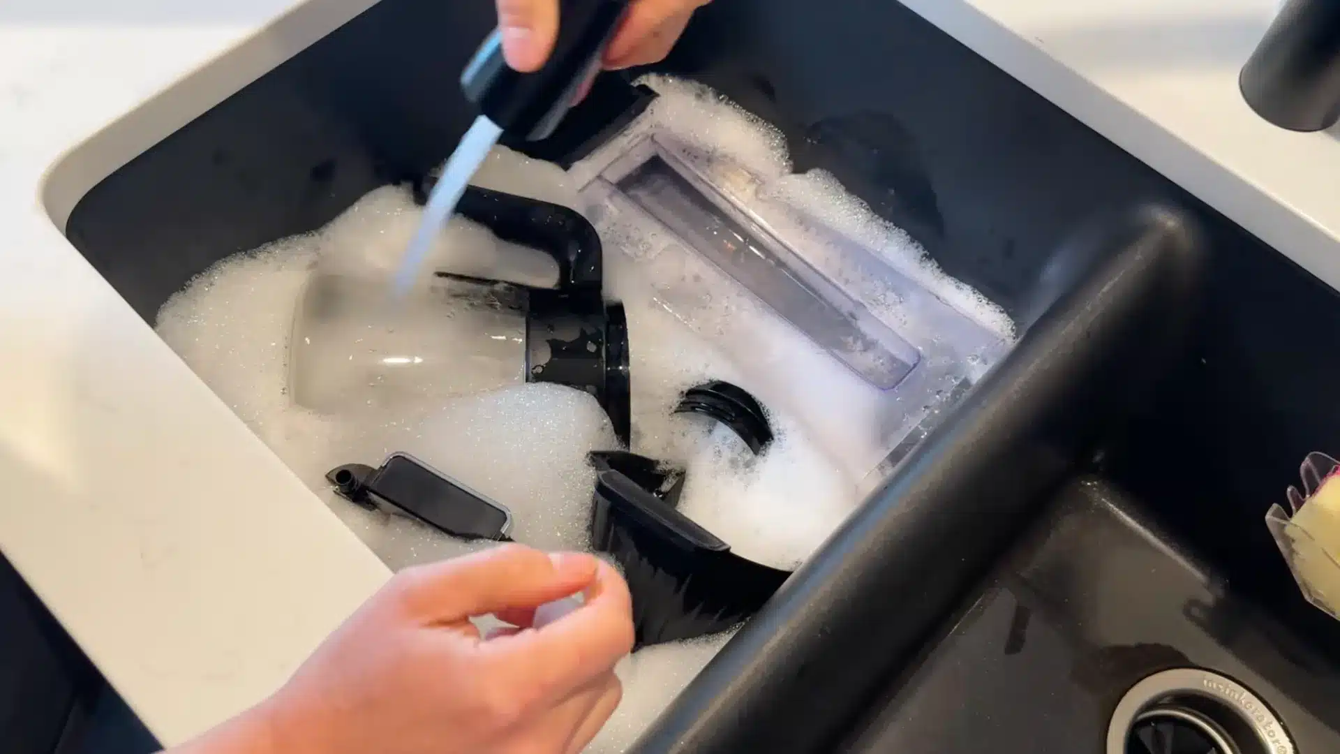 Washing removable coffee maker parts in soapy sink water during deep cleaning process