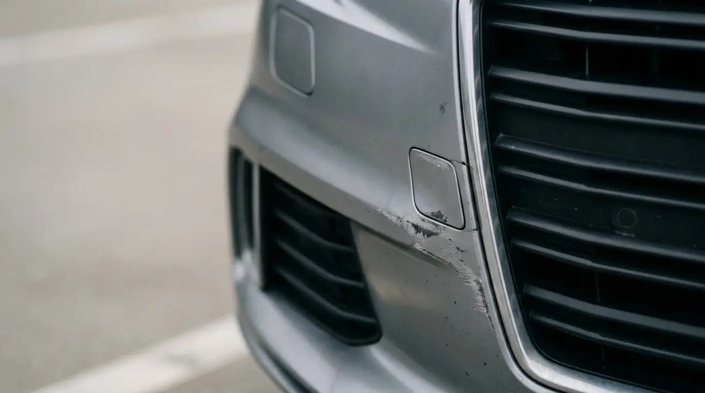 Close-up of scratched car front bumper with visible paint damage in a parking area.