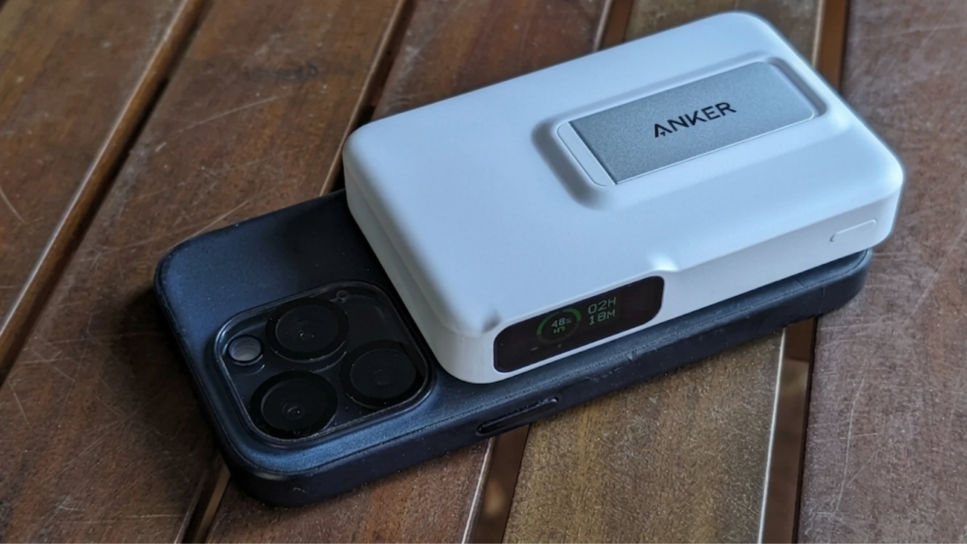 Anker magnetic power bank with digital battery display attached to the back of an iPhone on a wooden table