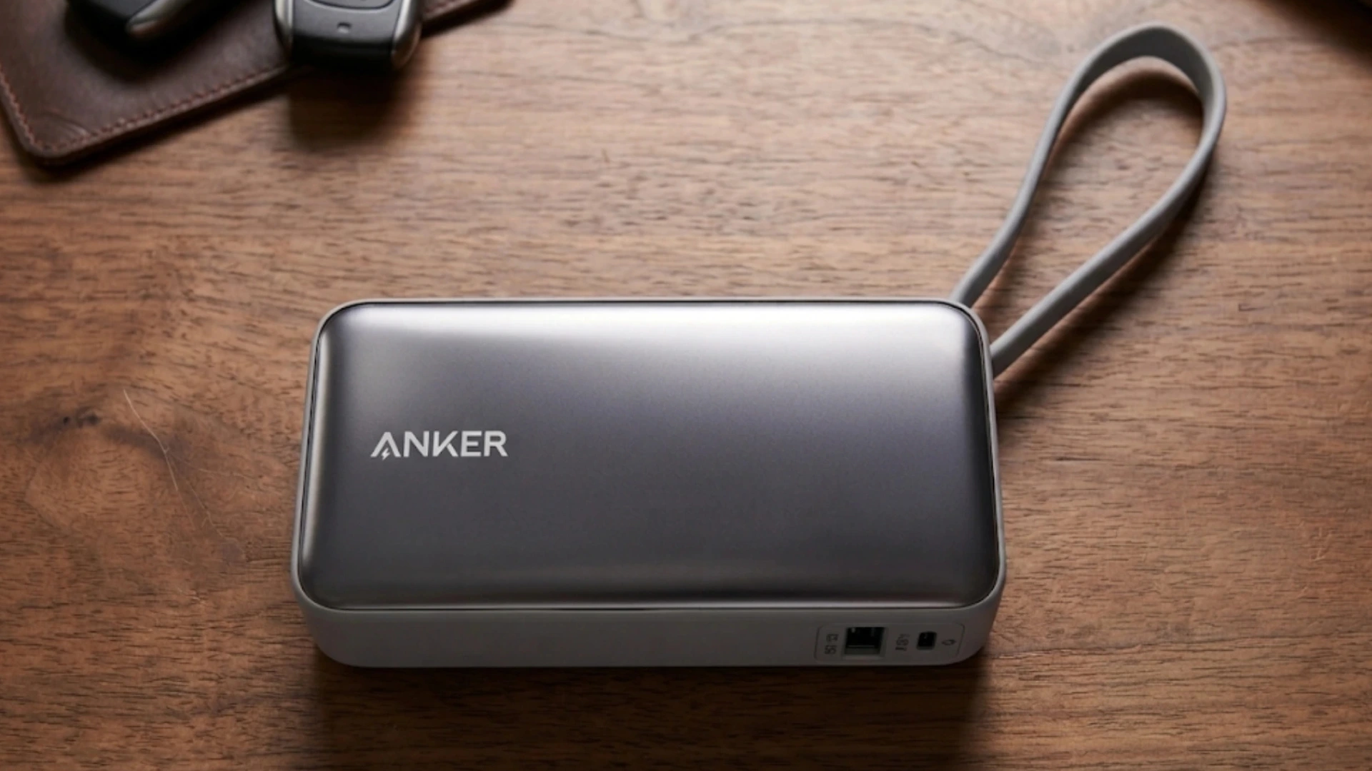 Anker power bank with built-in loop cable placed on a wooden desk beside car keys and a wallet