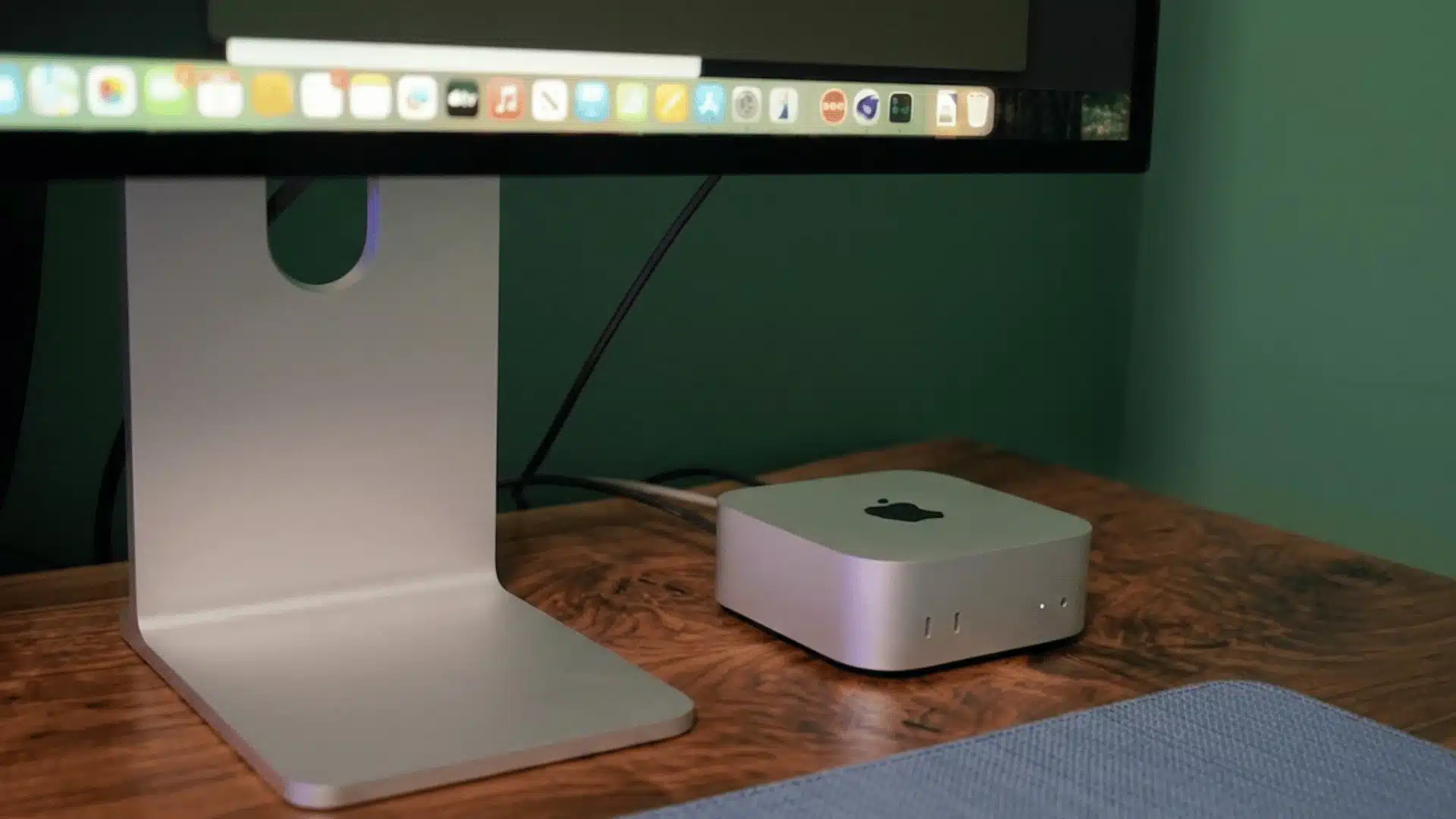 Apple Mac Mini on a wooden desk beside a monitor stand in a minimalist workspace setup