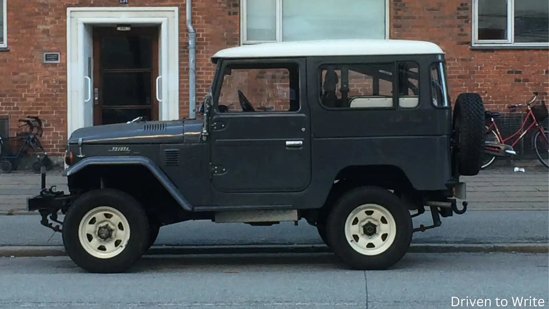 Classic black Toyota Land Cruiser parked on a city street with white roof, vintage styling, and brick building background