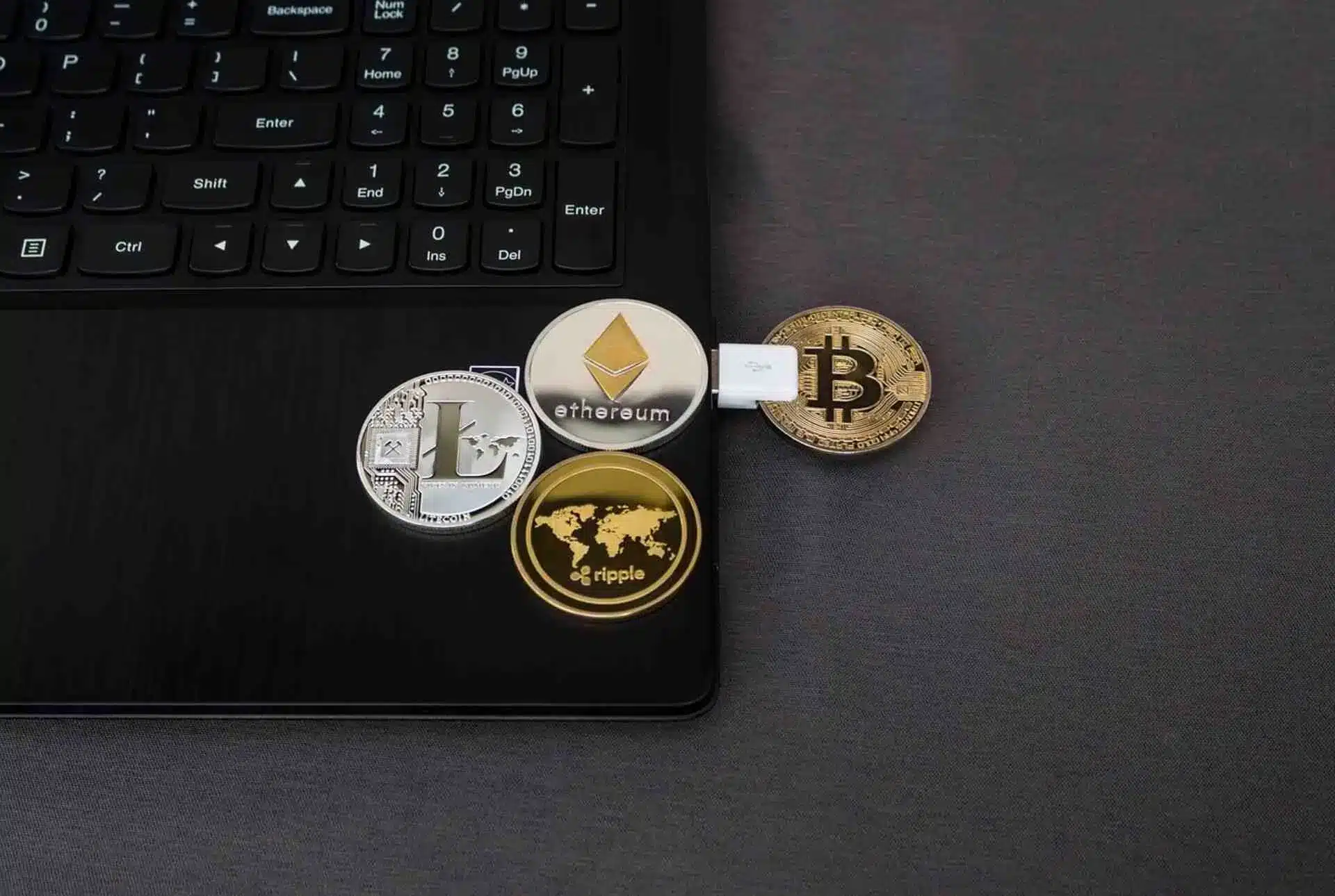 Cryptocurrency coins connected to laptop via USB on dark surface