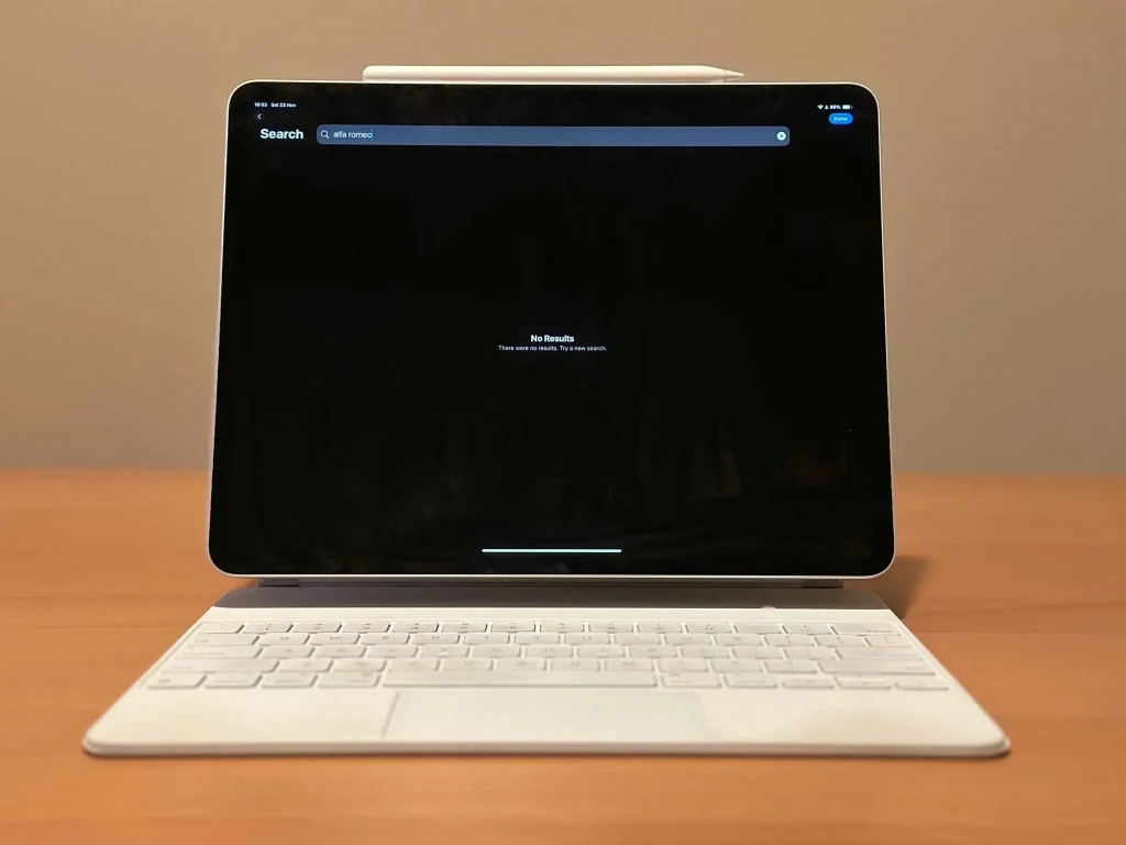 Tablet with search bar displayed, placed on wooden desk with attached white keyboard