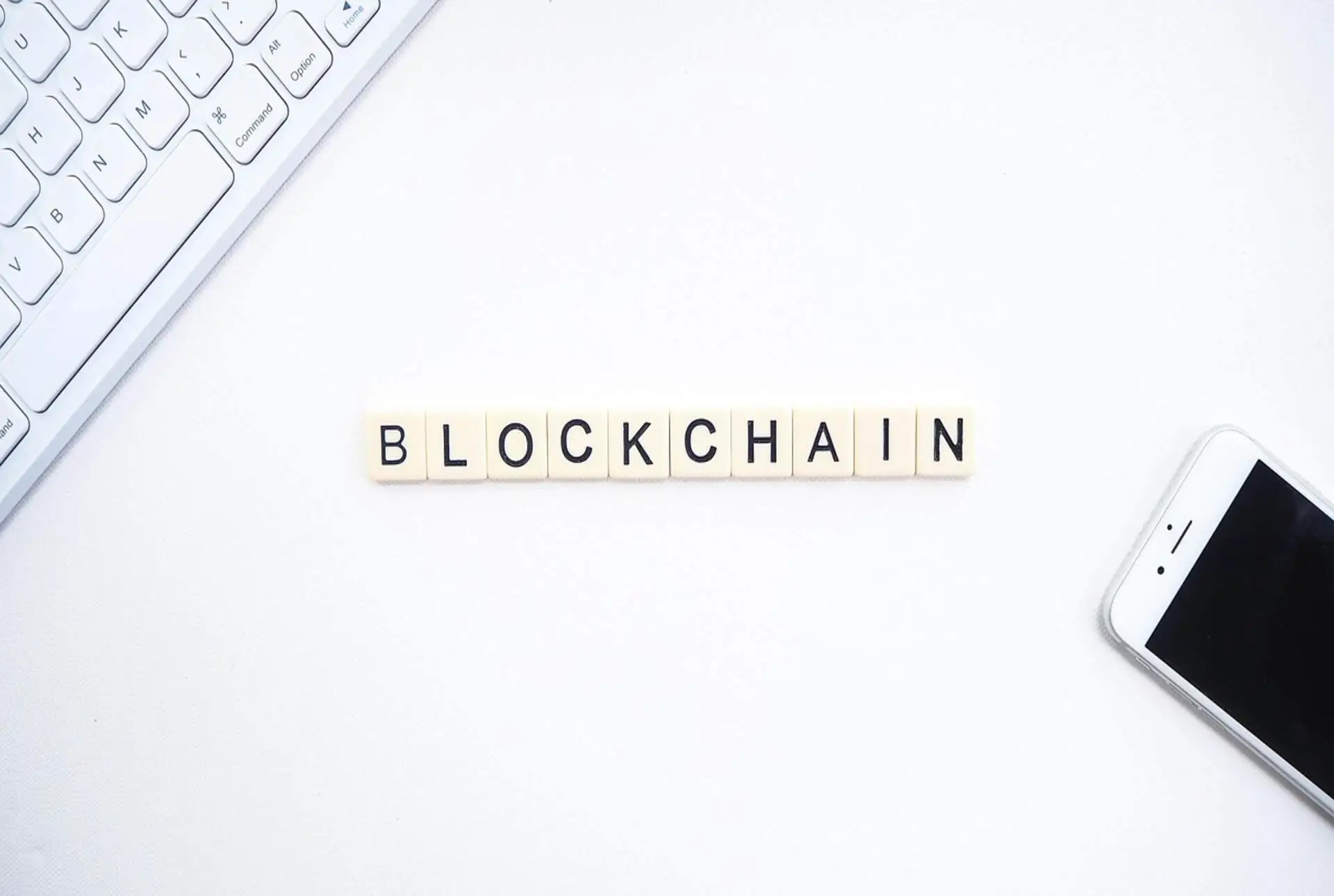 Keyboard, smartphone, and letter tiles spelling "BLOCKCHAIN" on white surface
