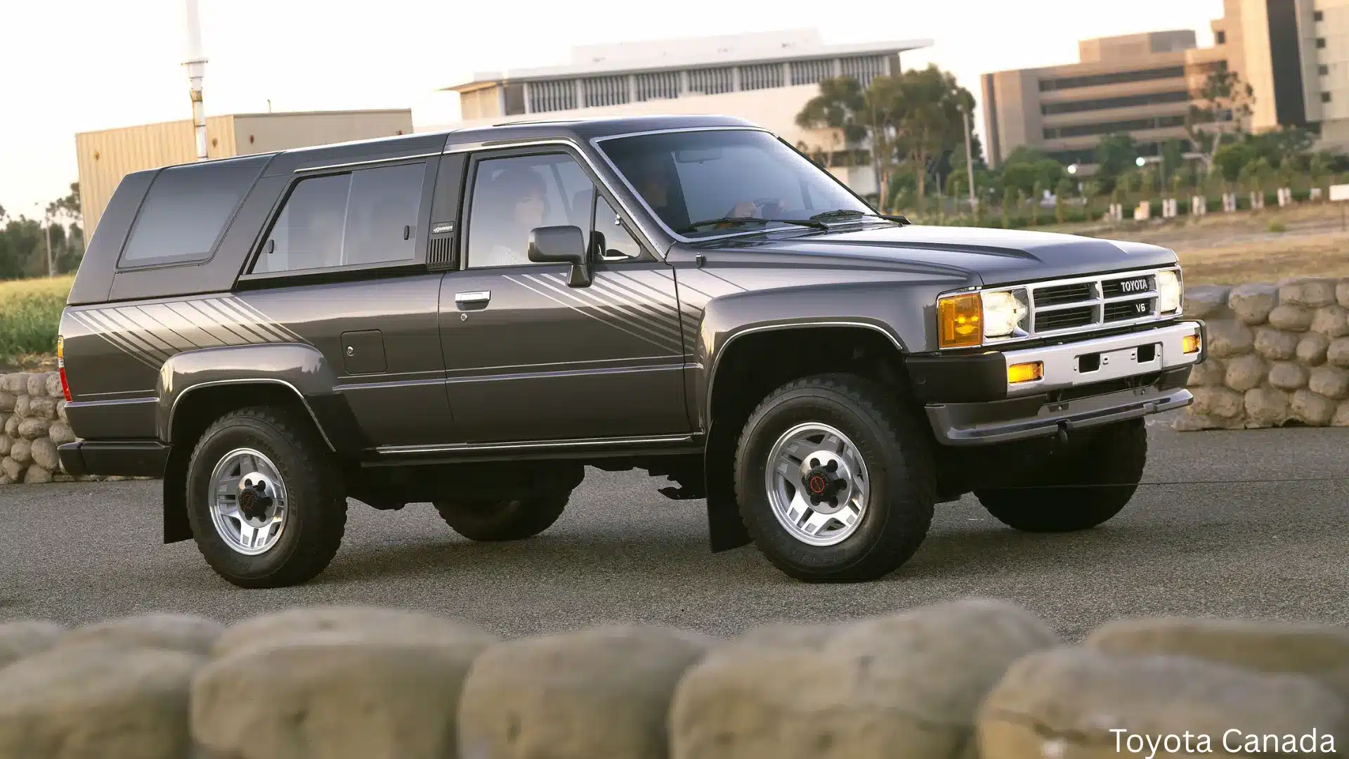 Gray vintage Toyota SUV with retro stripe graphics parked outdoors near office buildings during sunset
