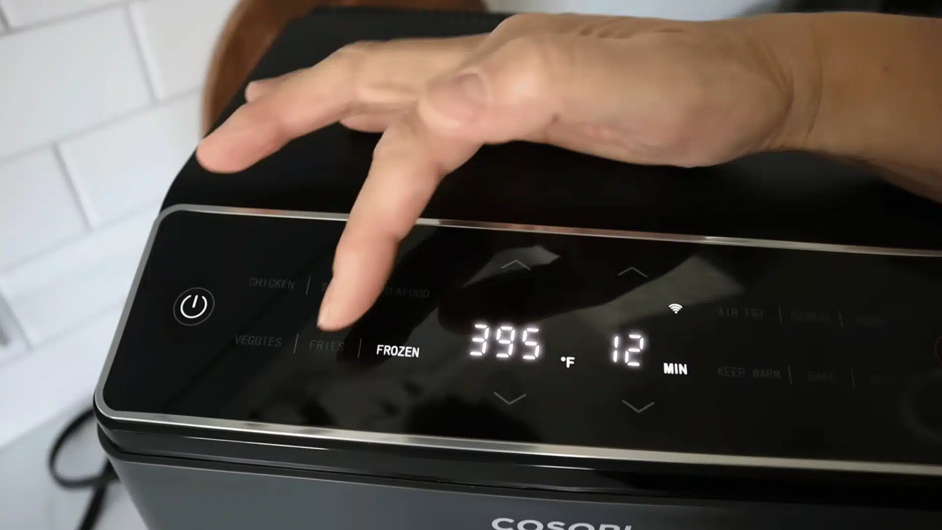 Hand adjusting Cosori air fryer frozen food setting at 395°F for 12 minutes