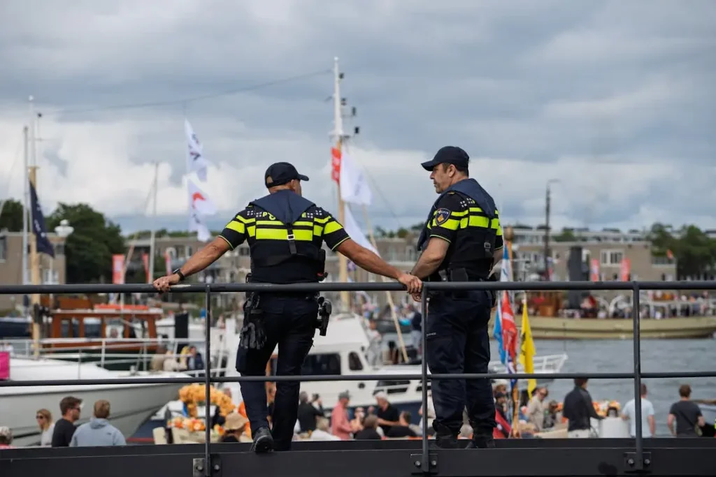 Two uniformed police officers standing on a waterfront railing, observing boats and people below