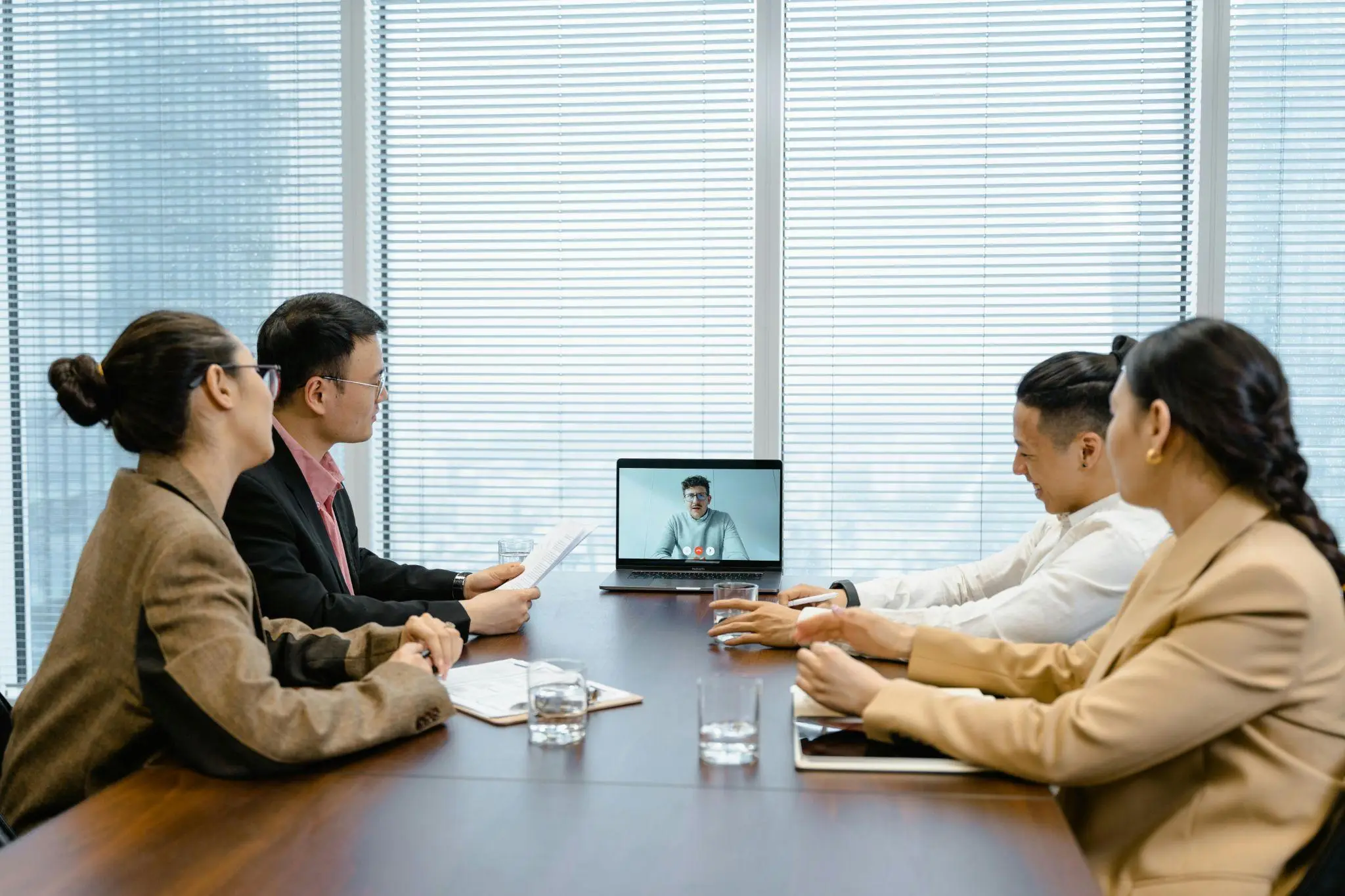 Four people in a conference room attending a video call on a laptop