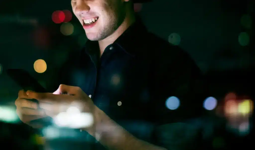 Person smiling while using smartphone in dark room with colorful bokeh lights