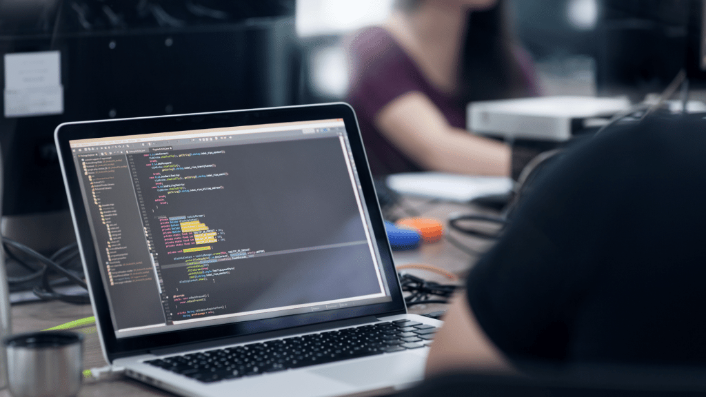 person coding on laptop with software development screen in modern office workspace with blurred background
