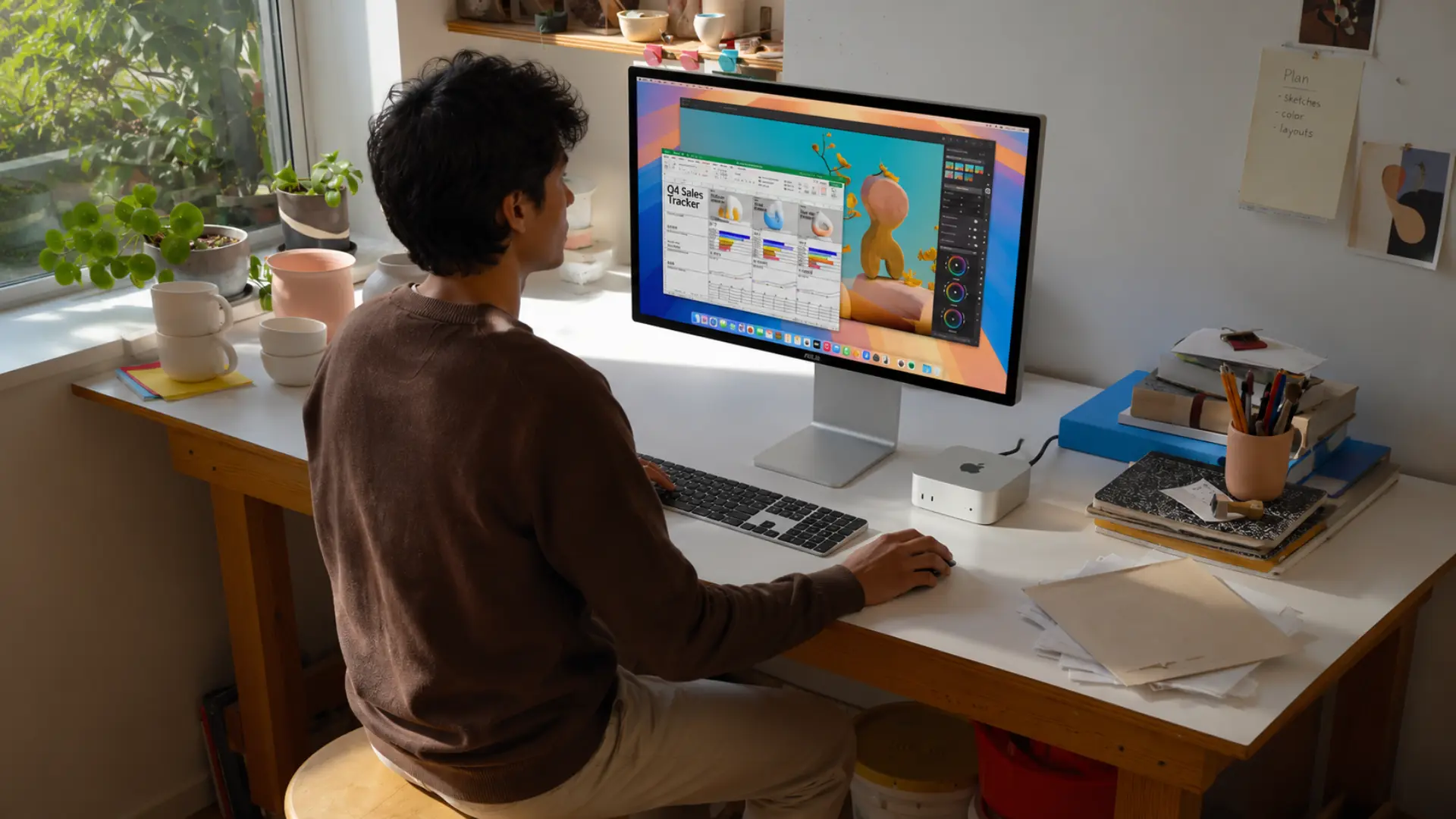 Person working at a bright home office desk with monitor, Mac mini, plants, and creative workspace setup