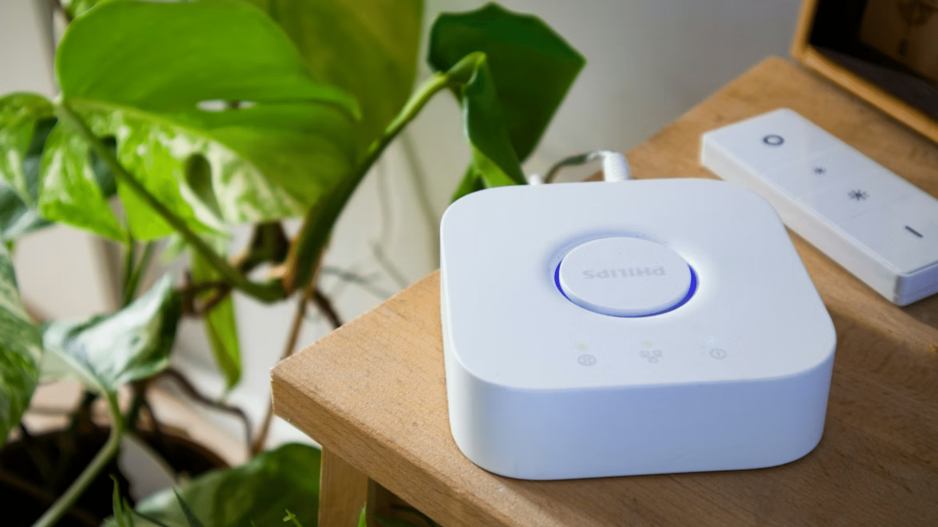 Philips Hue Bridge, the central hub for Philips Hue smart lighting systems, resting on a wooden table beside a minimalist remote control.