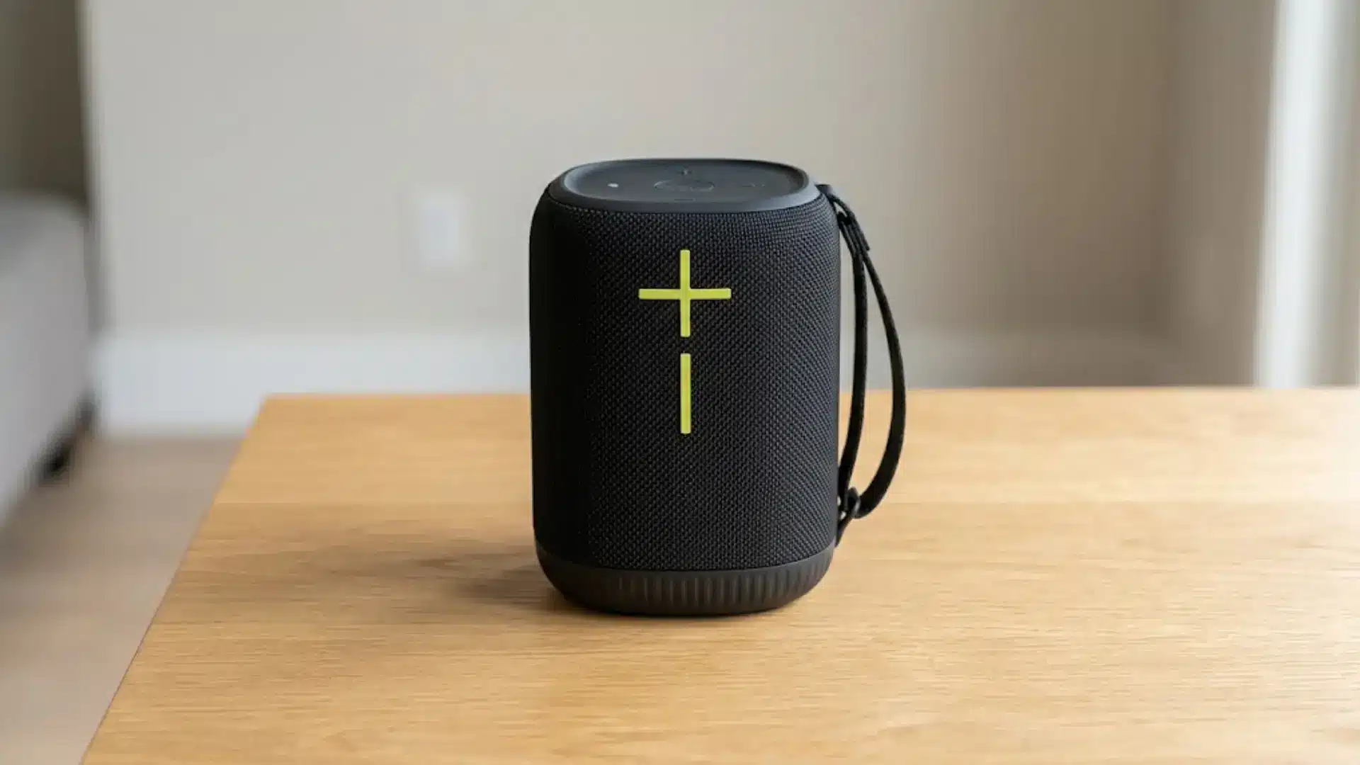 Portable Bluetooth speaker on table with bold plus symbol, compact design, indoor setting
