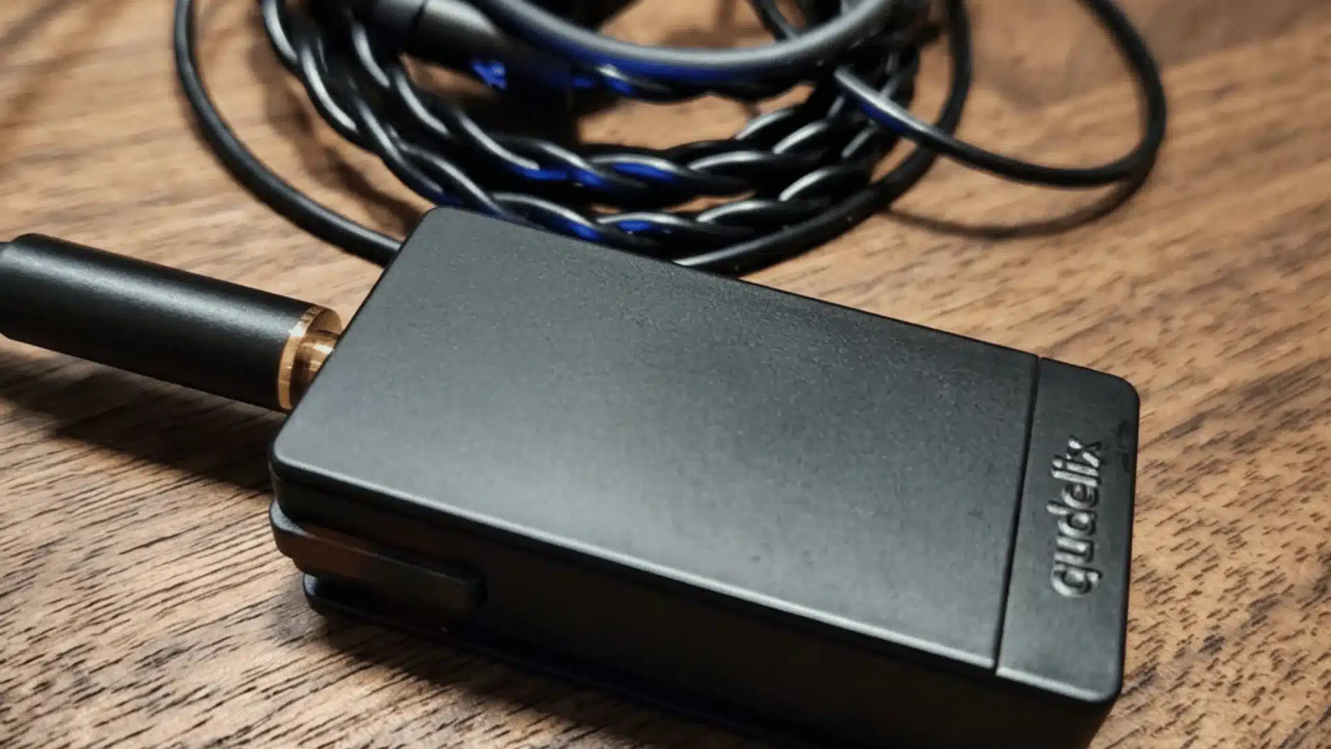 Qudelix 5K portable Bluetooth DAC:amp connected to wired IEMs on a wooden desk