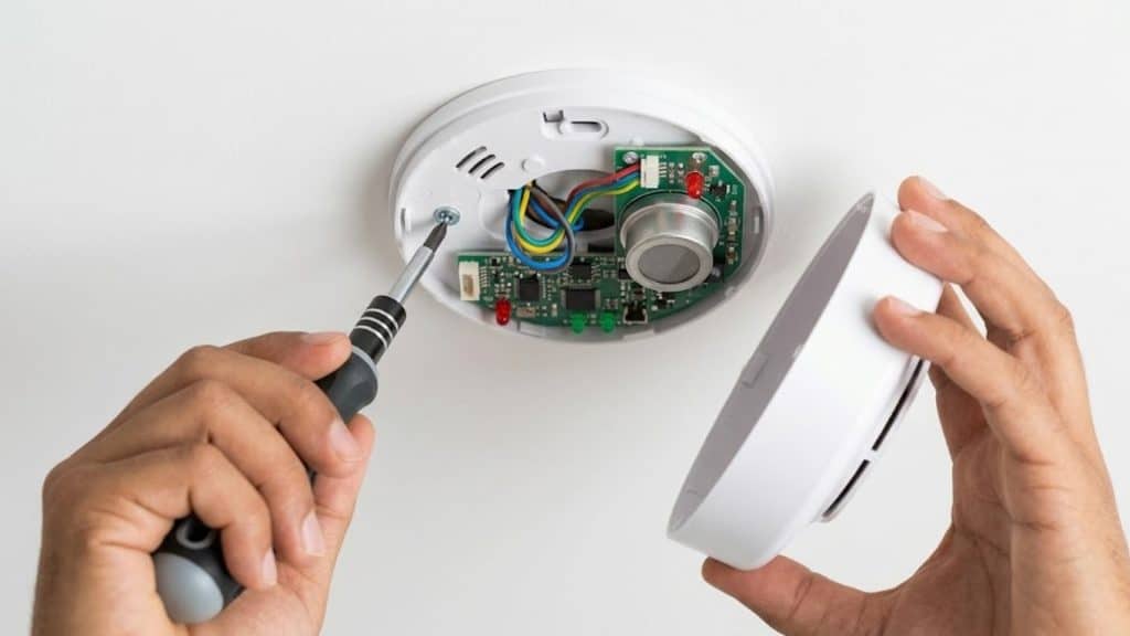 Technician opening a smoke detector during fire alarm maintenance and safety inspection at home