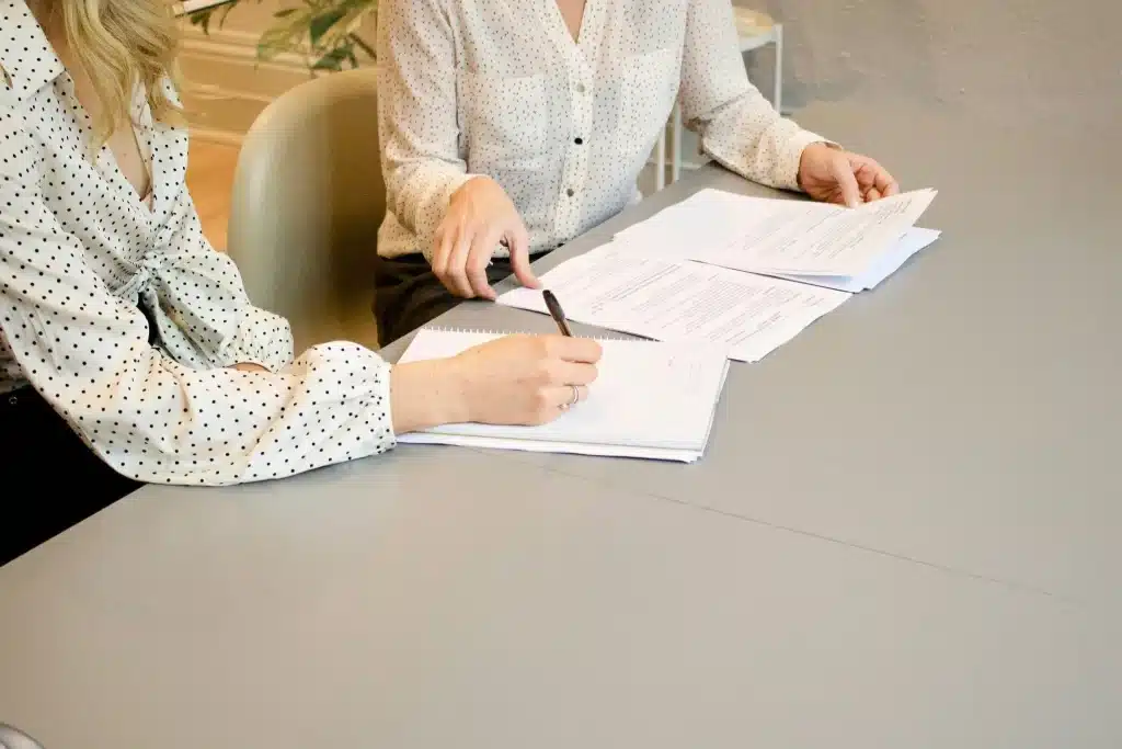 Two people reviewing documents at a gray office table with notepads and pens