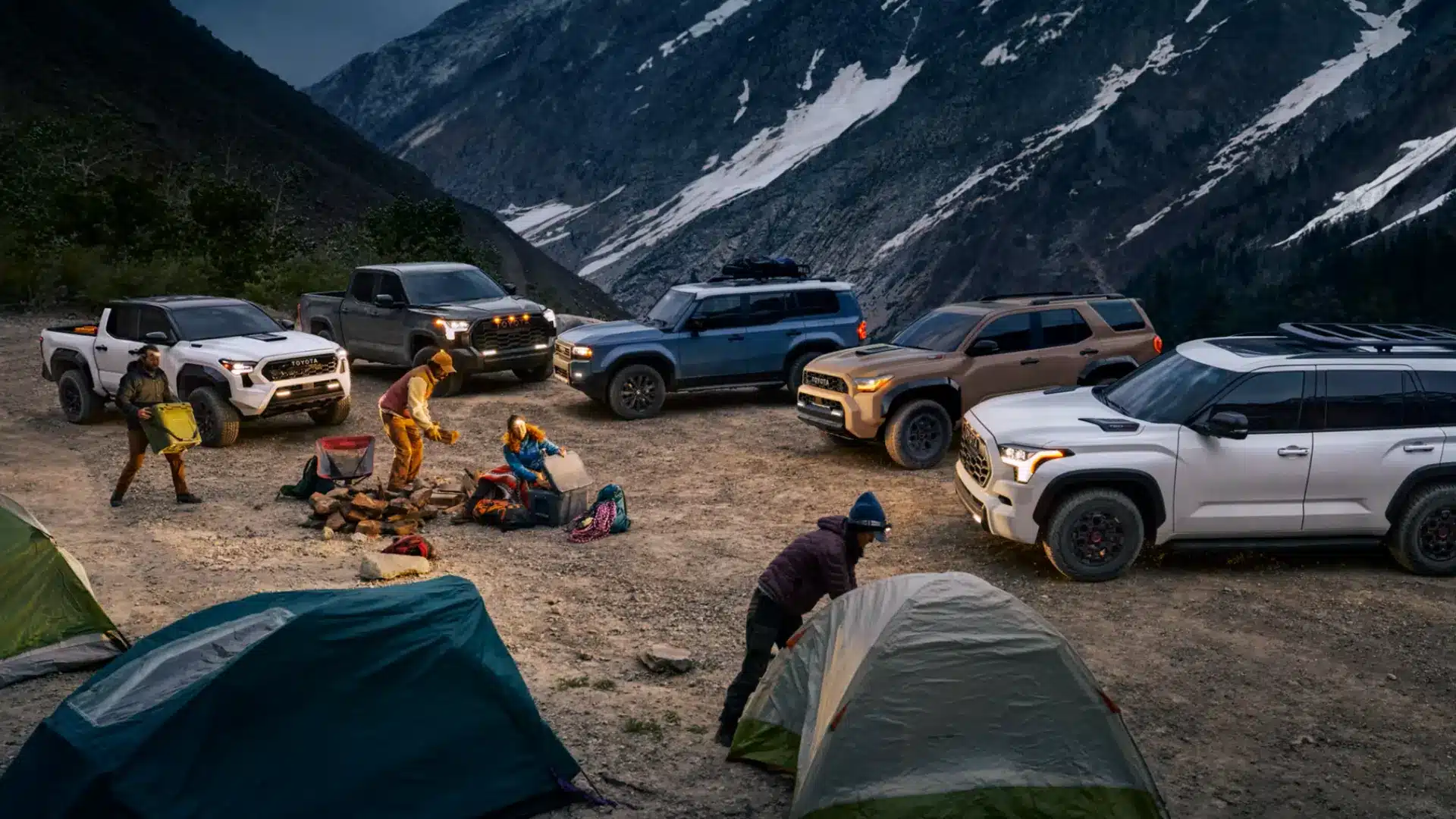 Toyota trucks and SUVs parked at a mountain campsite with campers setting up tents beside rugged off-road vehicles