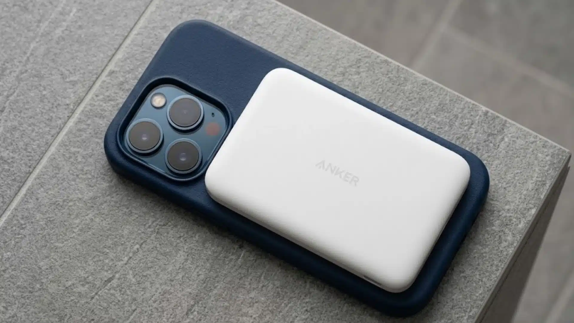 White Anker magnetic power bank attached to a blue iPhone case on a gray stone surface