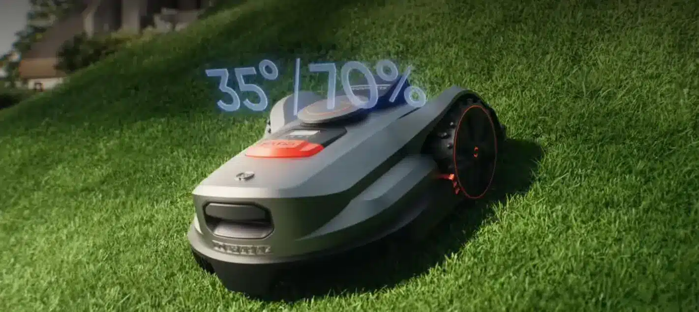 Robotic lawn mower operating on steep grassy hill in bright daylight