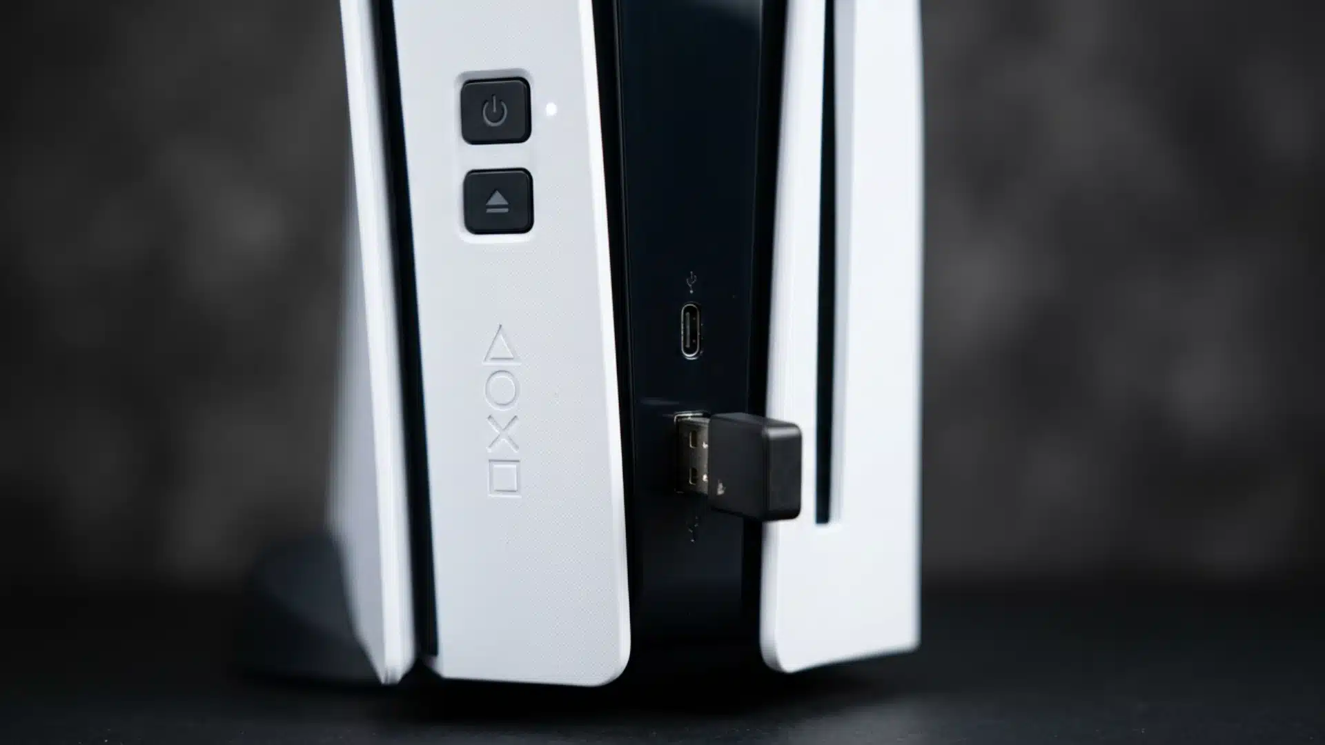 Close-up of a PS5 console with a USB Bluetooth adapter plugged into the front port for wireless headphone connectivity