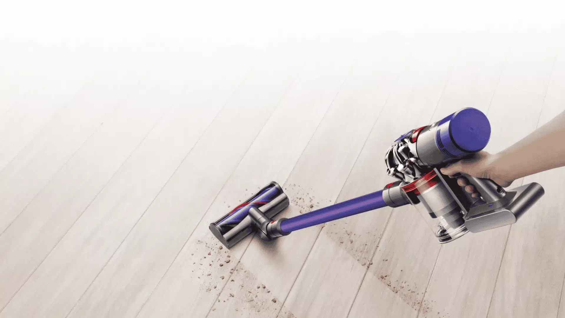 Dyson V7 cordless vacuum cleaning crumbs on a light wood floor with official product styling