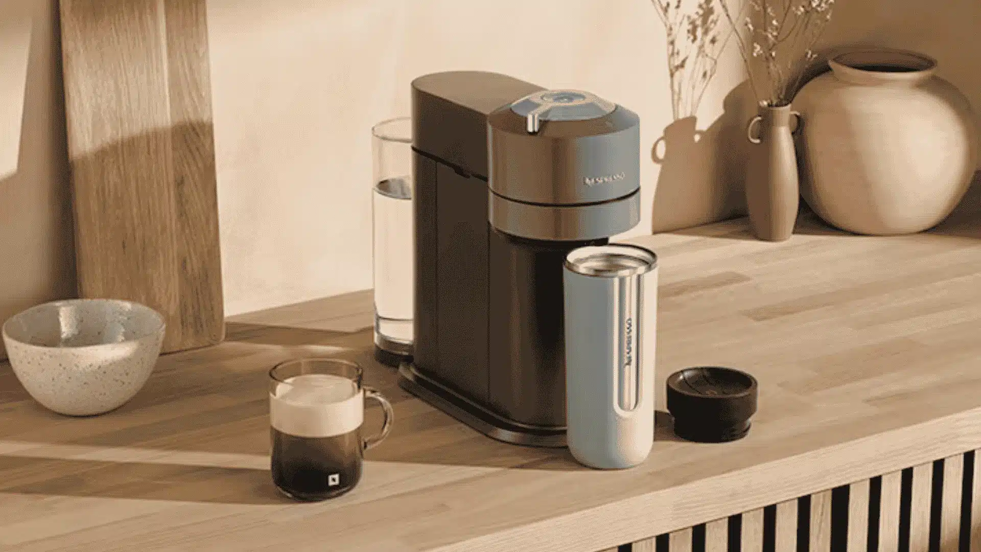 Nespresso Vertuo Next coffee machine with travel mug and coffee cup on a wooden kitchen counter with decor in the background