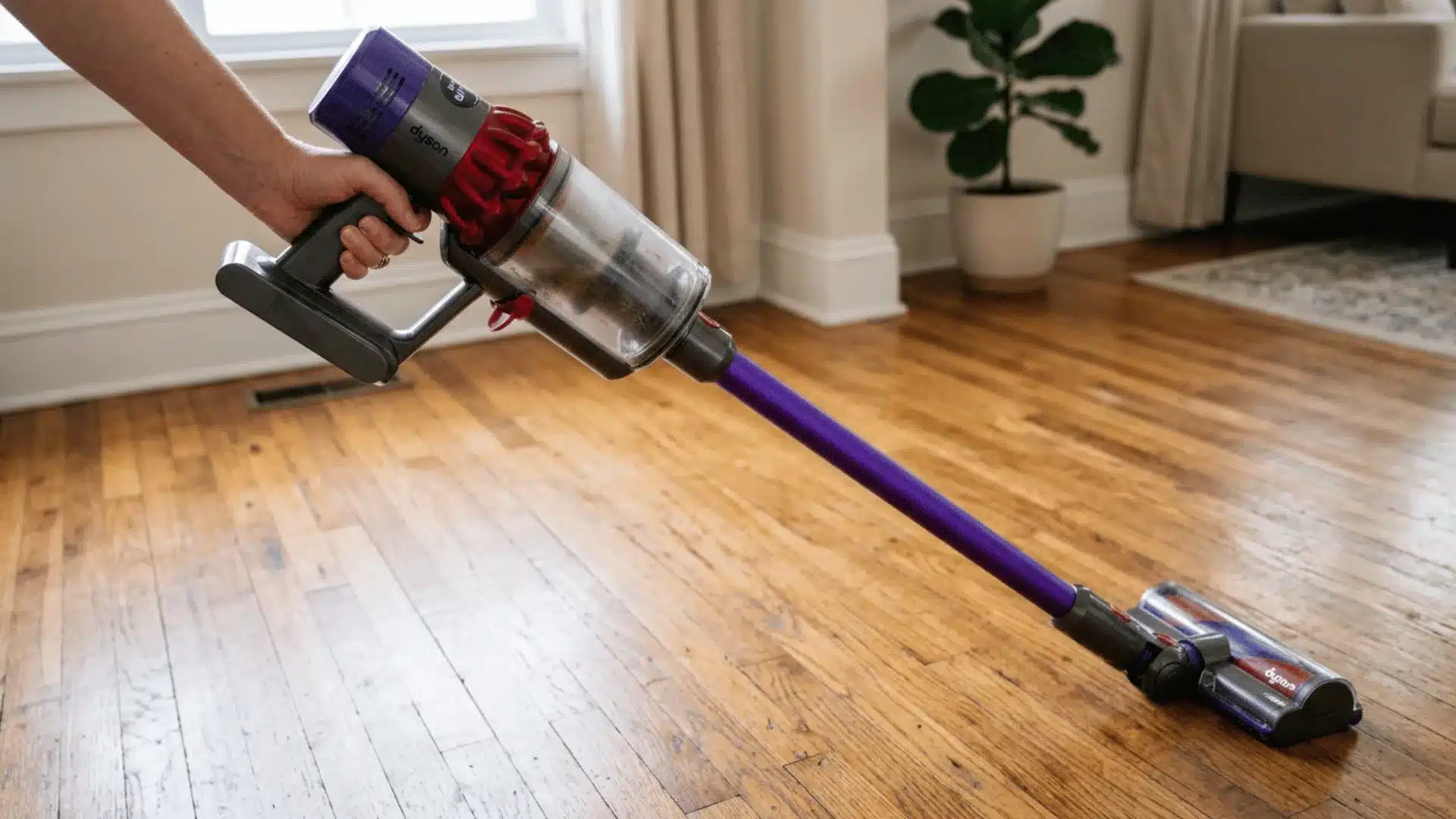 Person using Dyson cordless vacuum on wooden floor in a living room, cleaning surface debris on floor surface