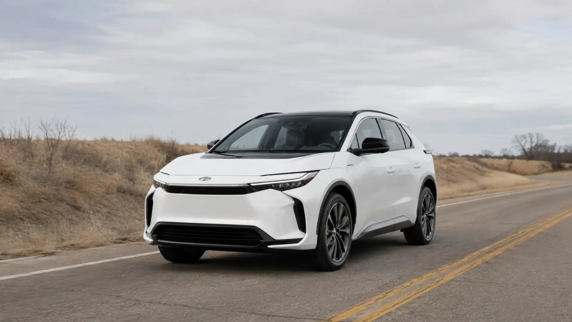 White Toyota bZ electric SUV driving on a minimal countryside road under an overcast sky