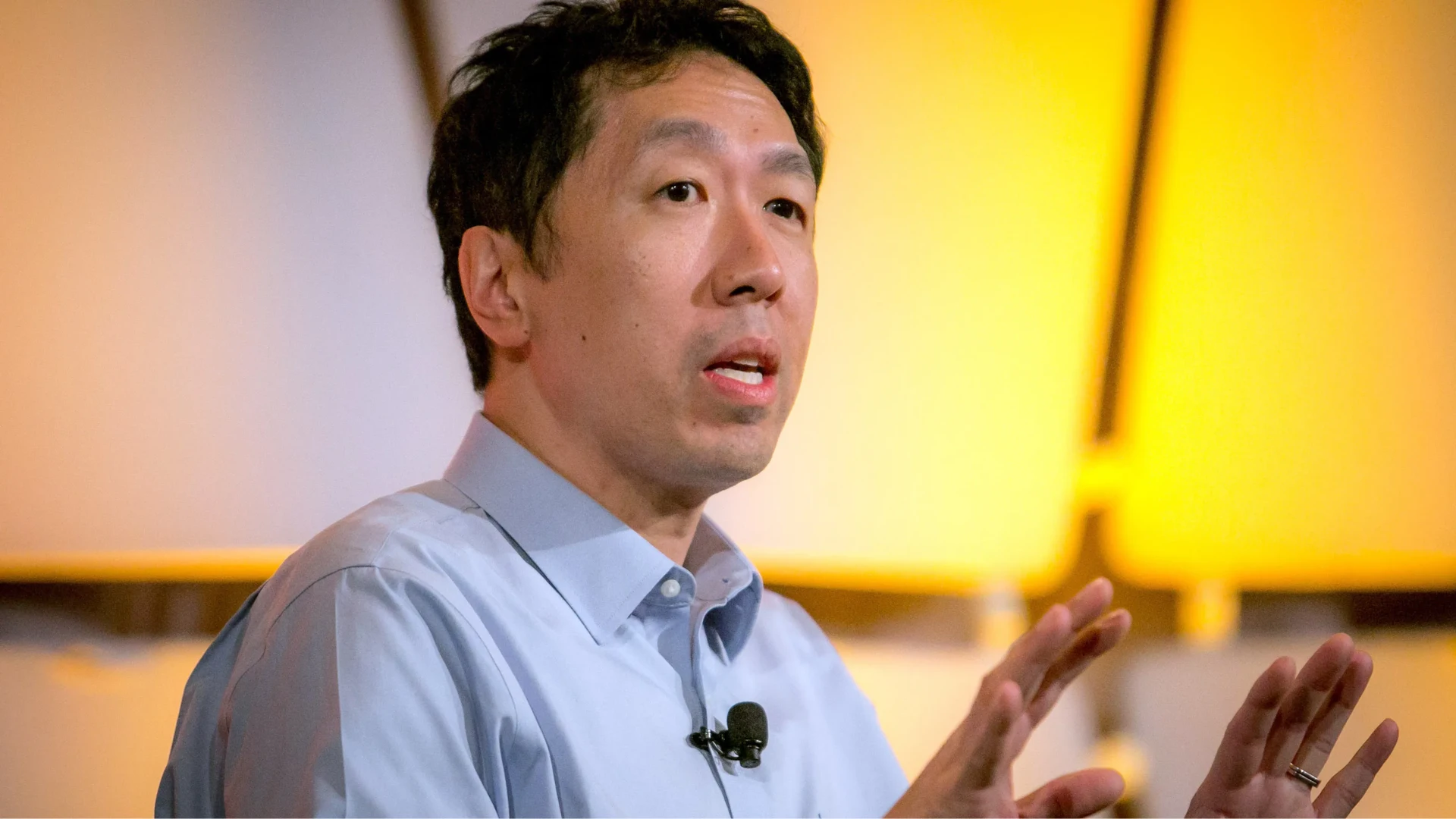 Andrew Ng on stage with a lapel microphone and warm yellow background