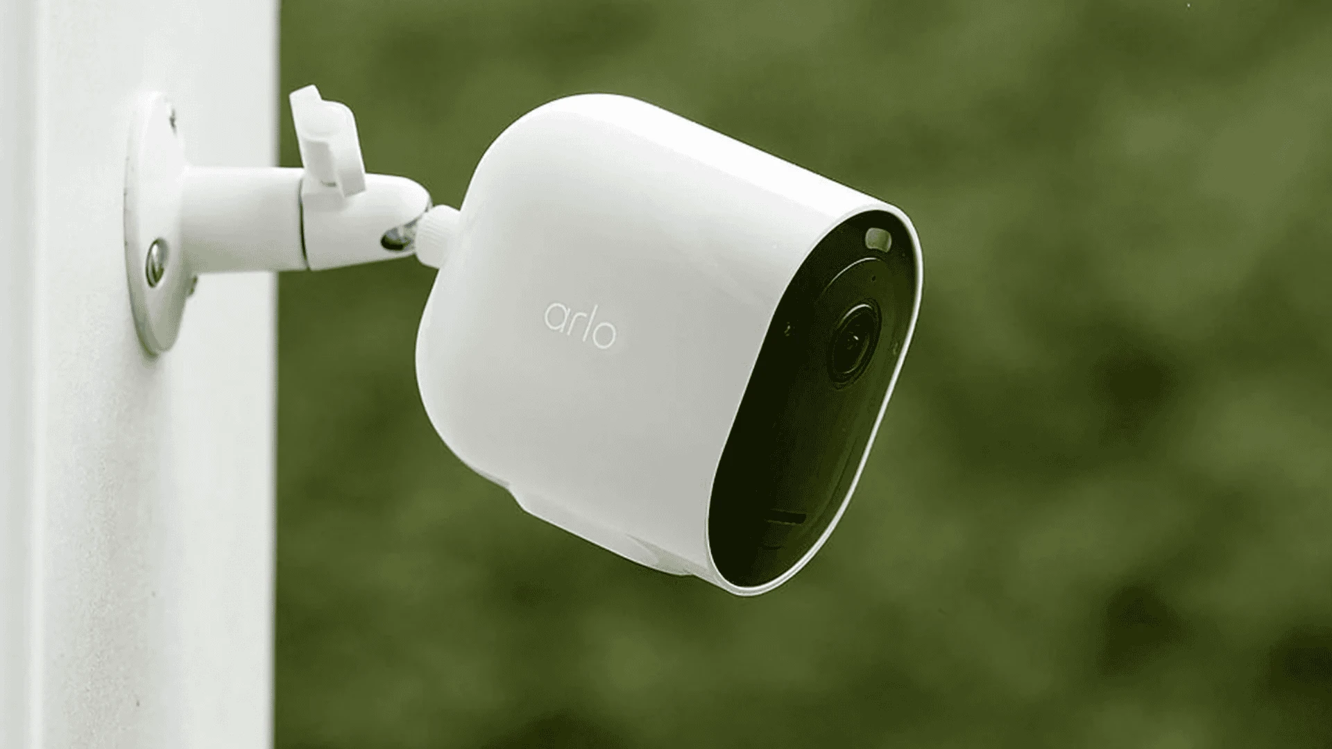 Arlo outdoor security camera mounted on a wall with a blurred green background for home monitoring