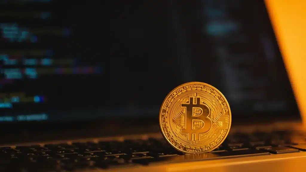 Bitcoin coin on laptop keyboard with blurred coding screen in warm light