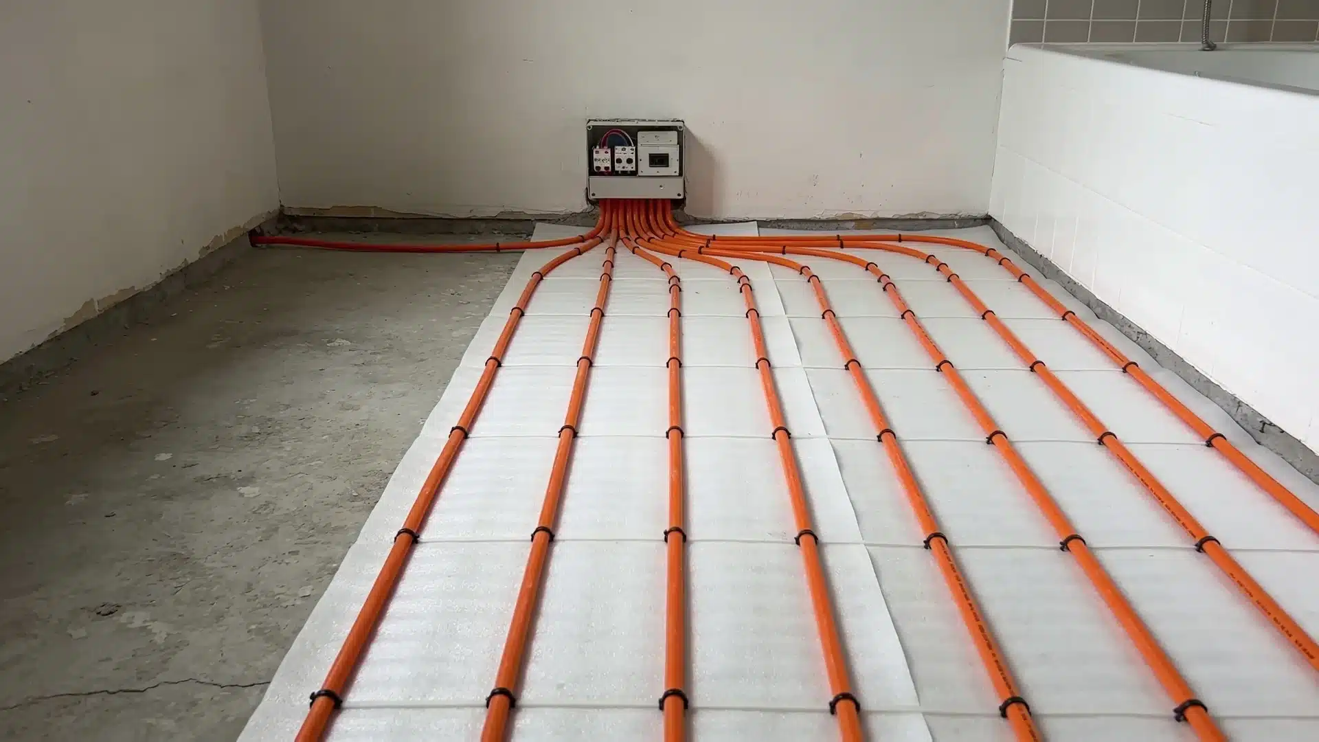 Electric radiant floor heating system installed beneath tile flooring with heating cables connected to a wall thermostat controller