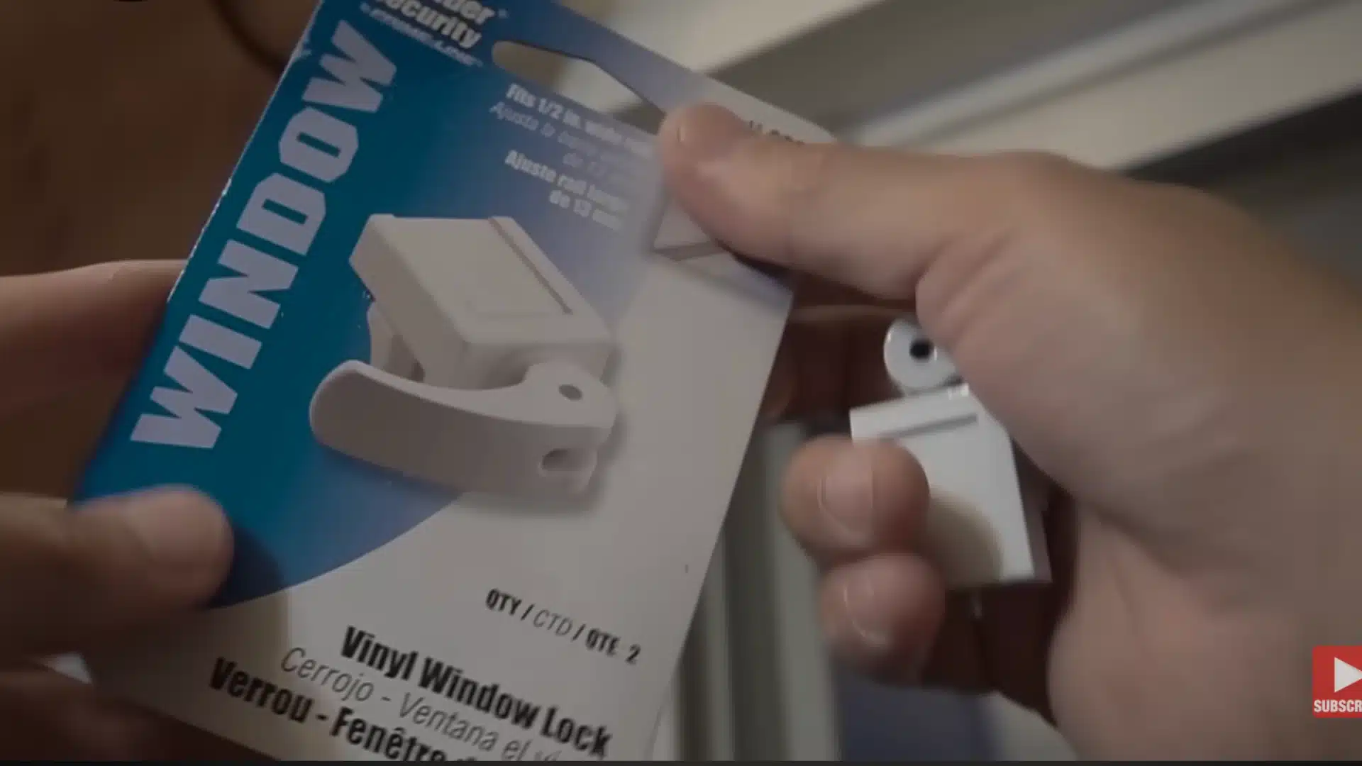 Hands holding a packaged Defender Security vinyl window lock