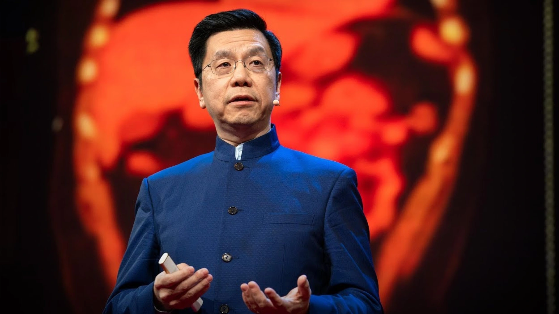Kai Fu Lee in a blue coat presenting on stage with a red screen behind him