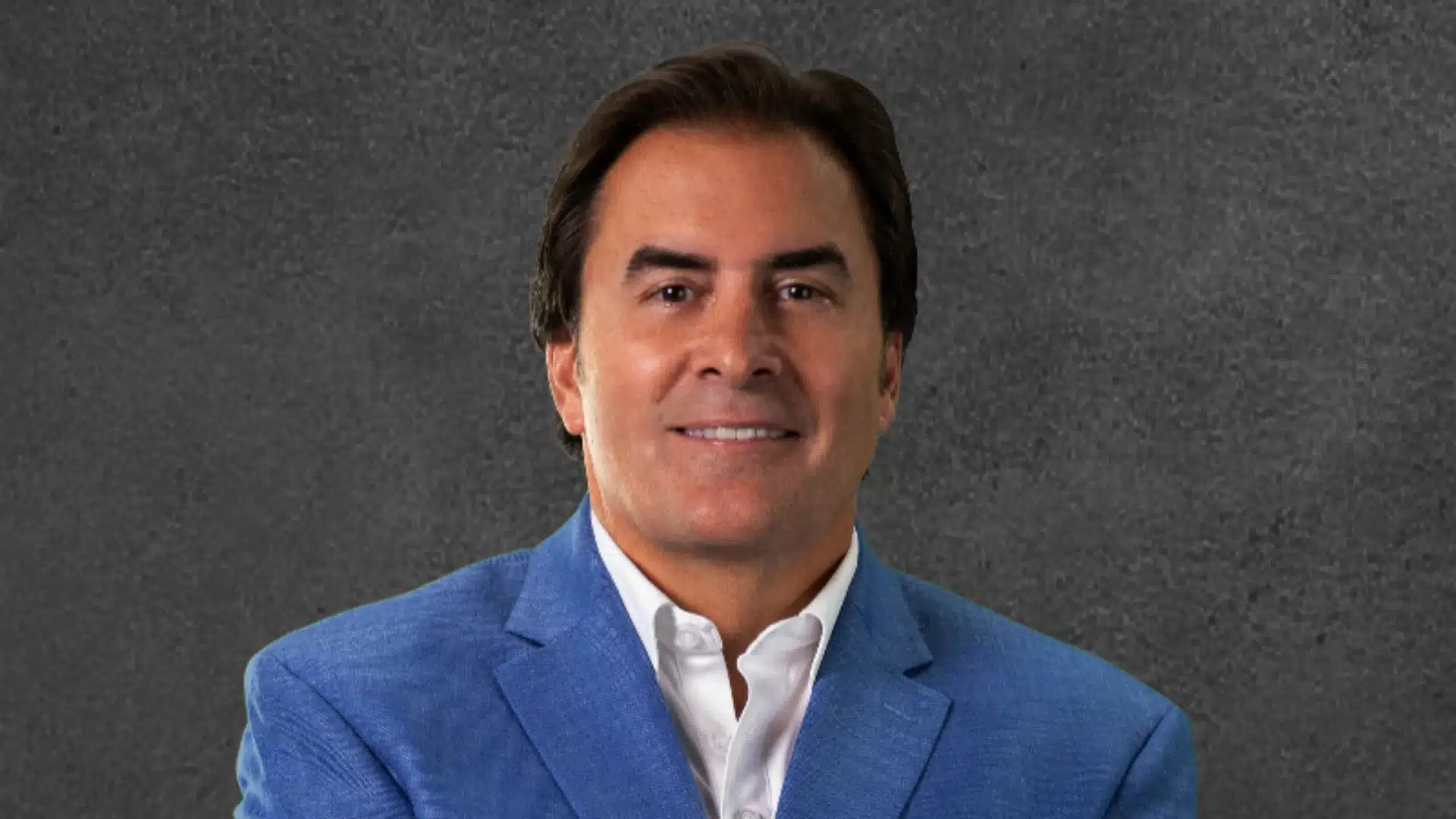 Mark Lynd in a blue suit smiling against a dark textured background