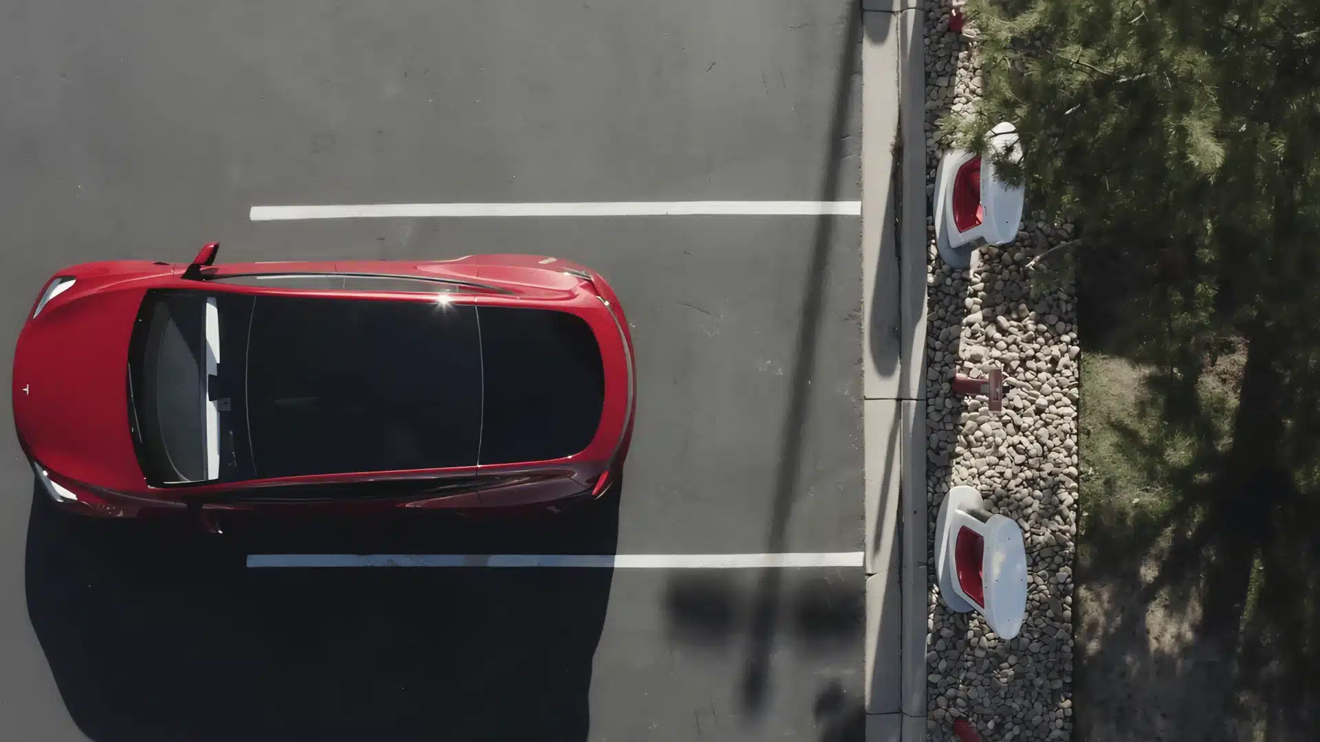 Red Tesla parked beside Supercharger stations in an empty parking lot