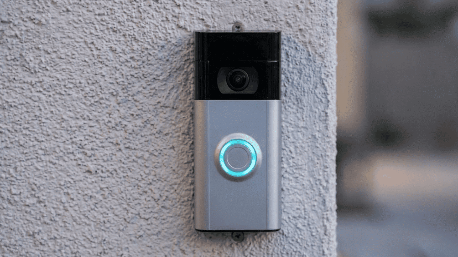 ring video doorbell mounted on an exterior wall with illuminated button indicating active status near home entrance