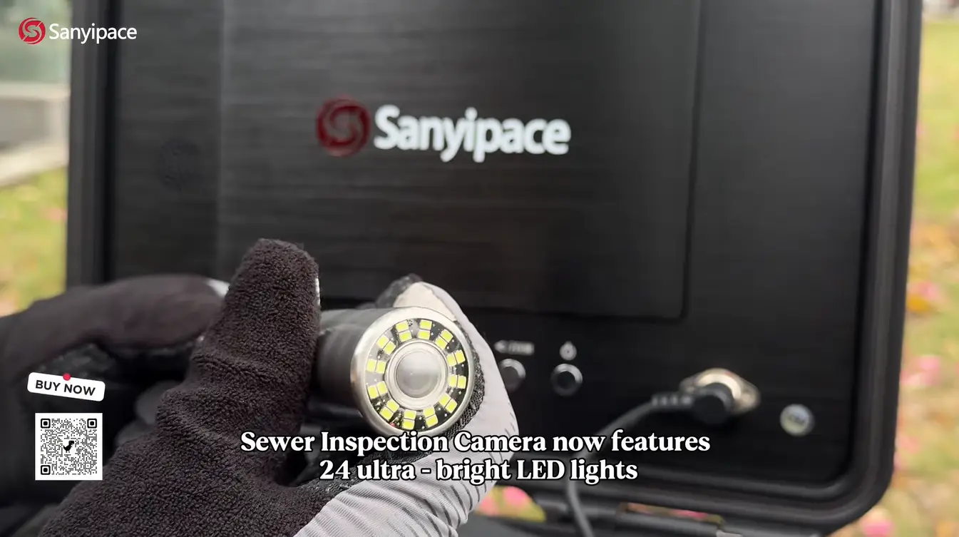 Gloved hand holding sewer inspection camera with LED lights in outdoor setting