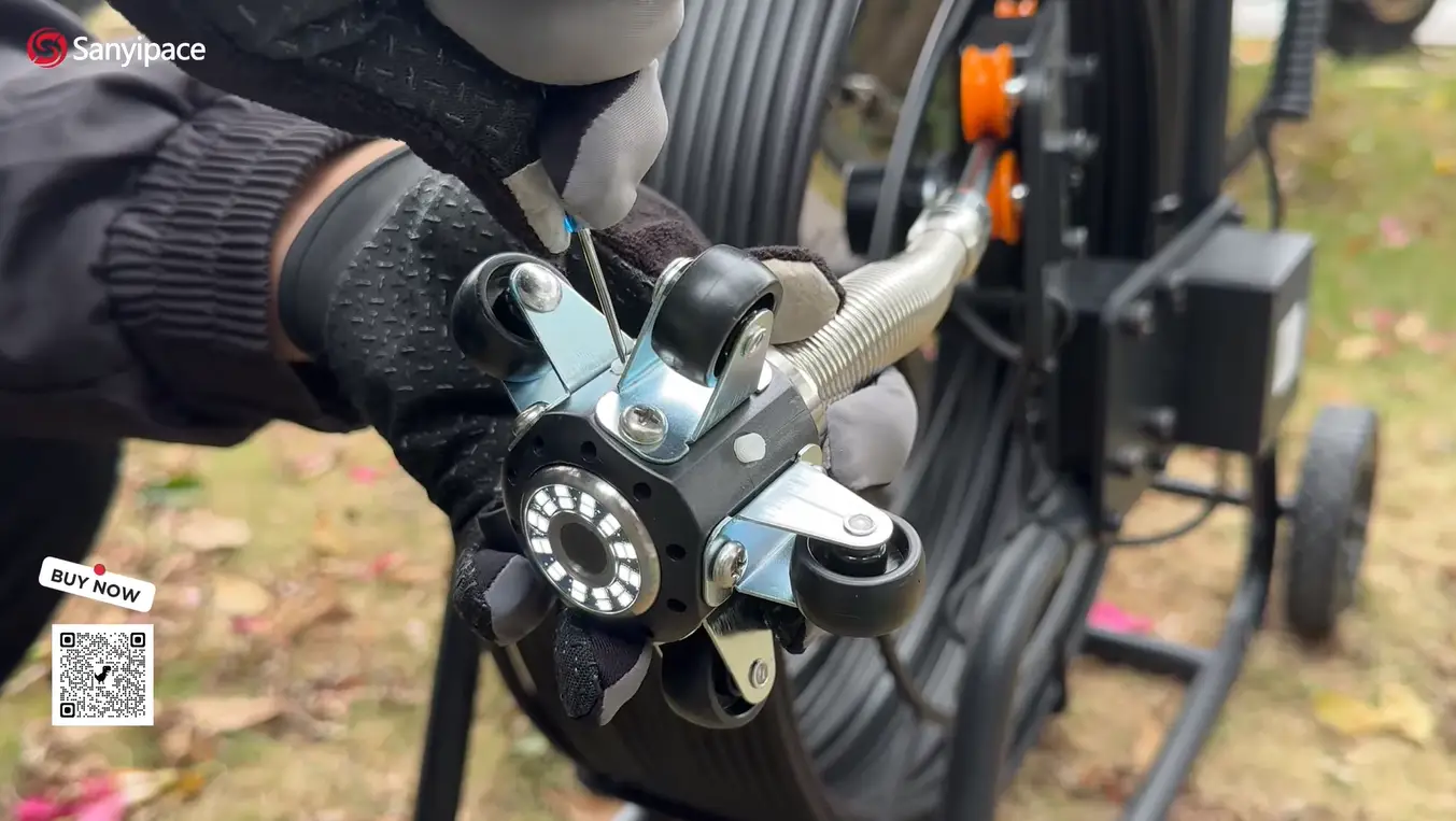 Gloved hands adjusting a camera on a sewer inspection cable outdoors