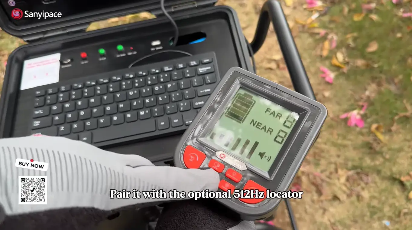 Hand holding digital locator remote next to open laptop outdoors with grassy background
