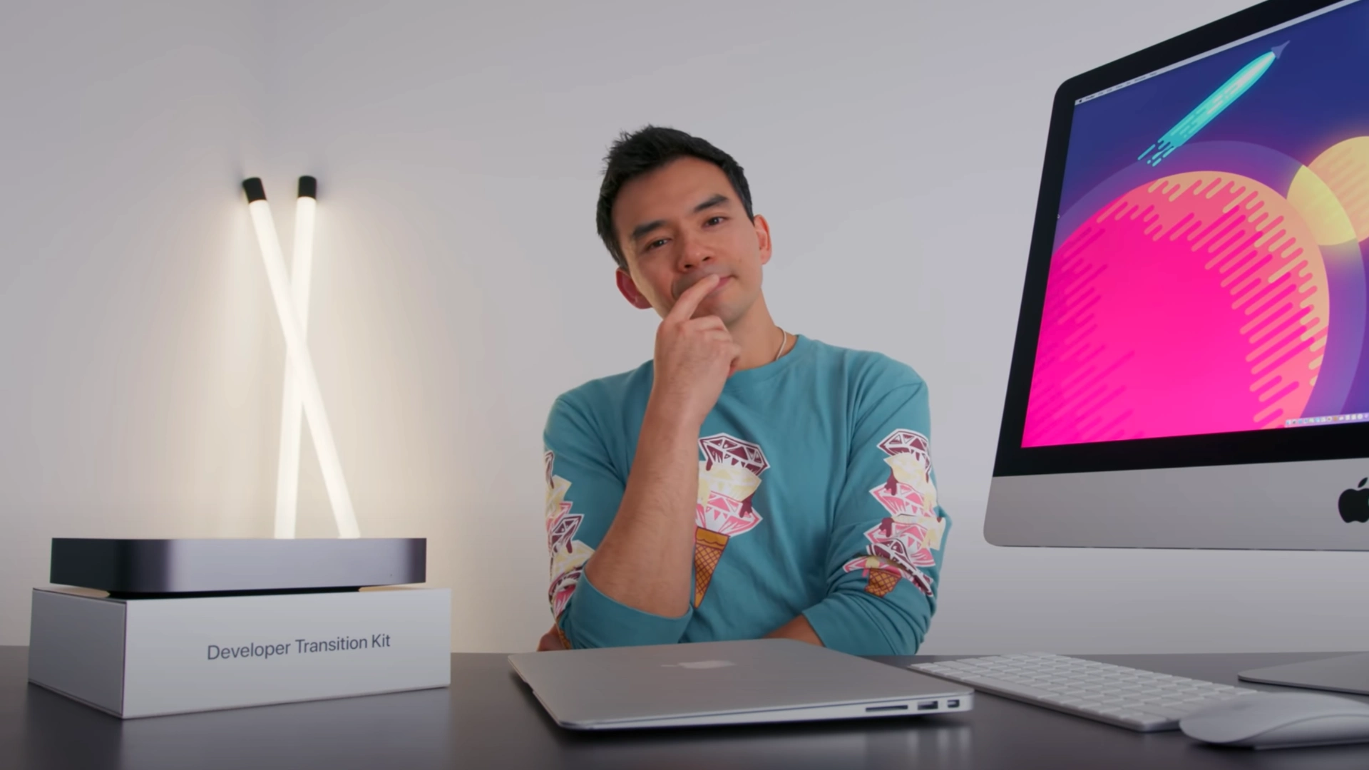 Tech creator Dave Lee seated at a desk with Apple devices and a colorful desktop display