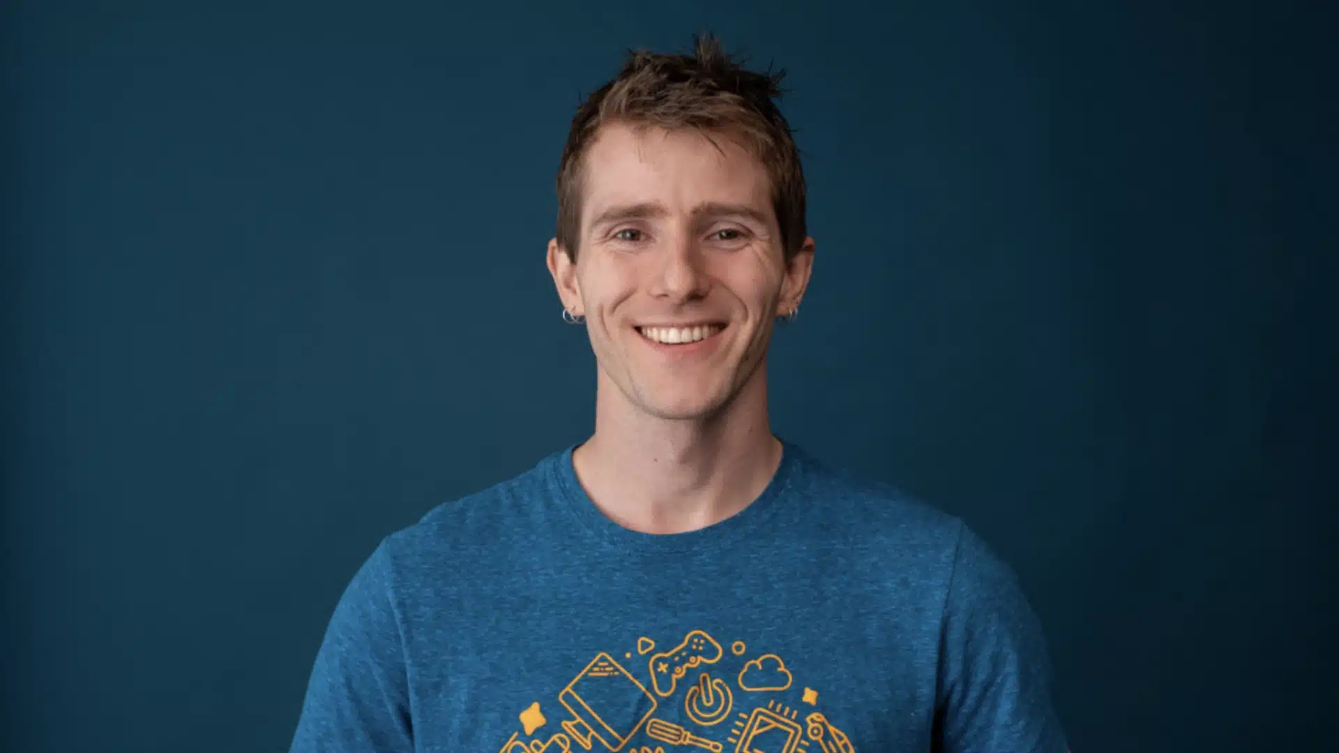 Tech creator Linus Sebastian in a blue shirt smiling against a dark studio background