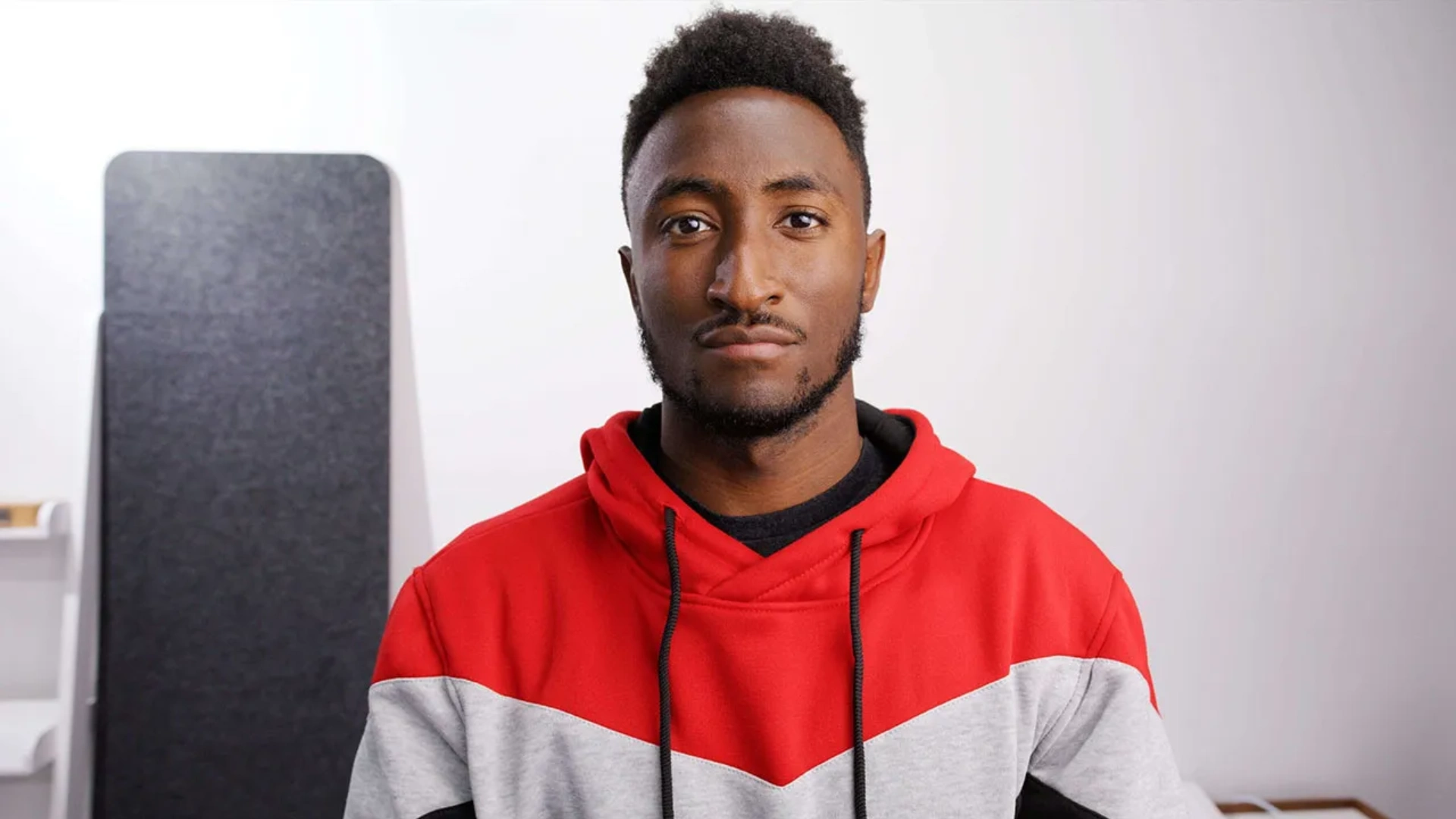 Tech creator Marques Brownlee in a red hoodie facing the camera in a bright studio setup