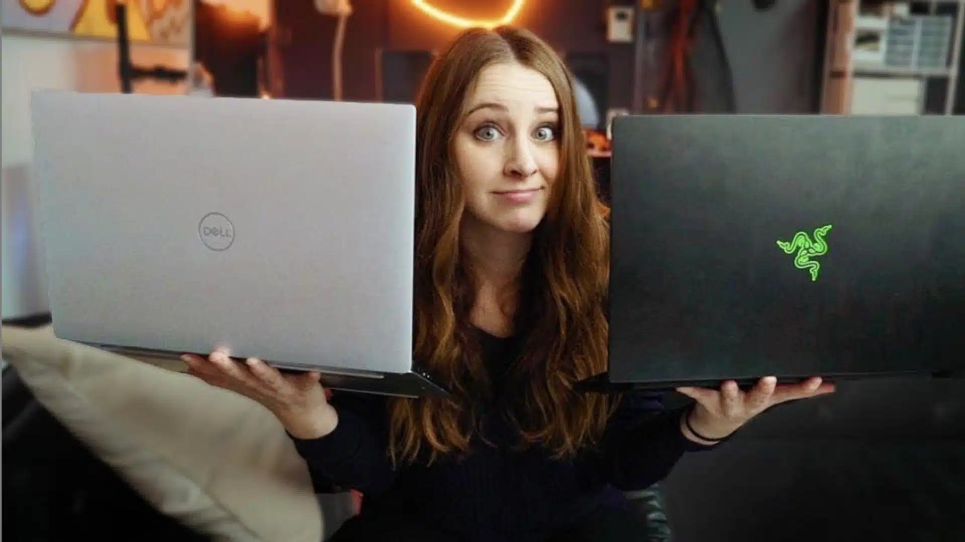 Tech creator Sara Dietschy holding two laptops for a product comparison in a home studio setup