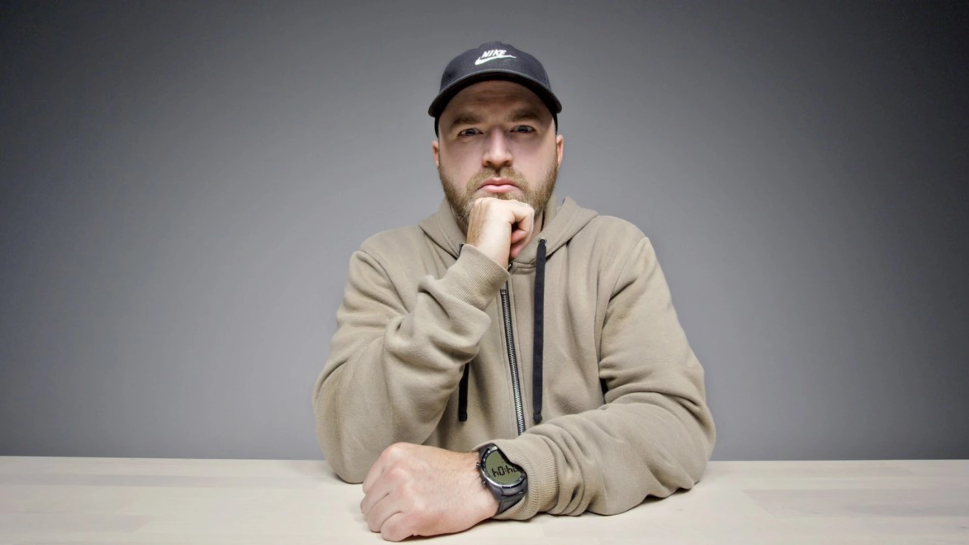 Tech creator Unbox Therapy in a cap and hoodie seated at a table against a gray studio background