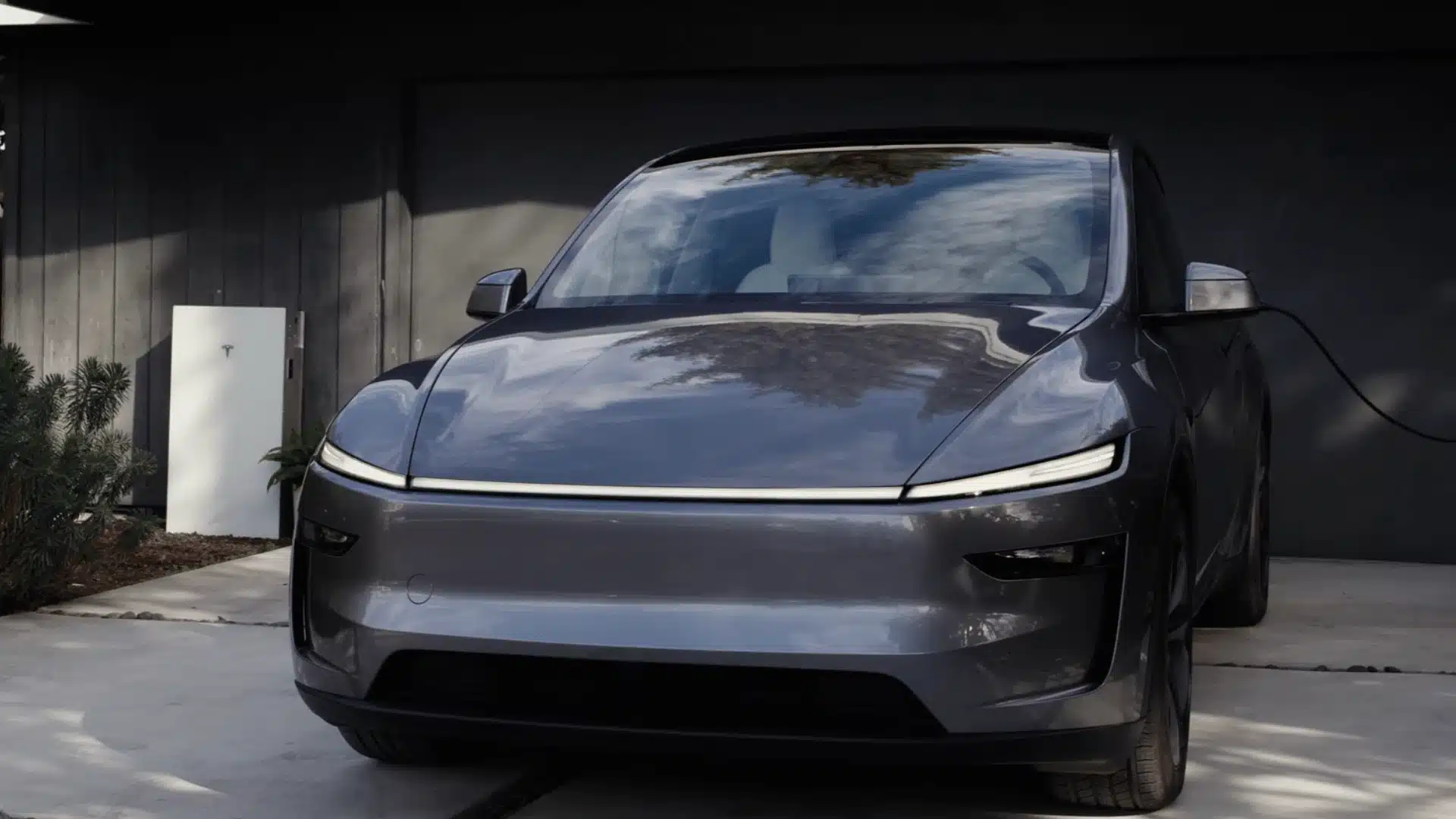 Tesla Cybercab charging in modern driveway beside Tesla Powerwall system